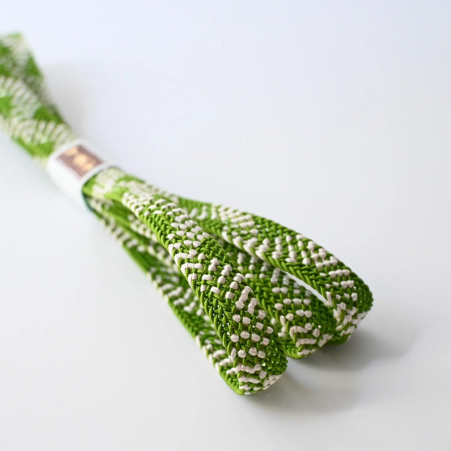 Close-up view of recycled silk obijime in a fresh matcha green with white accent.