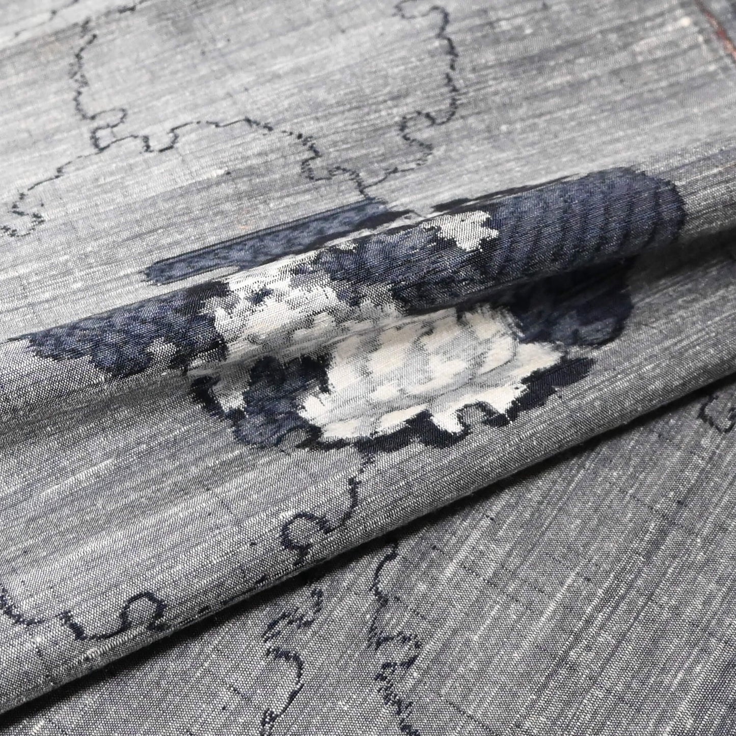 Close-up view of vintage grey tsumugi silk kimono fabric piece with floral pattern.