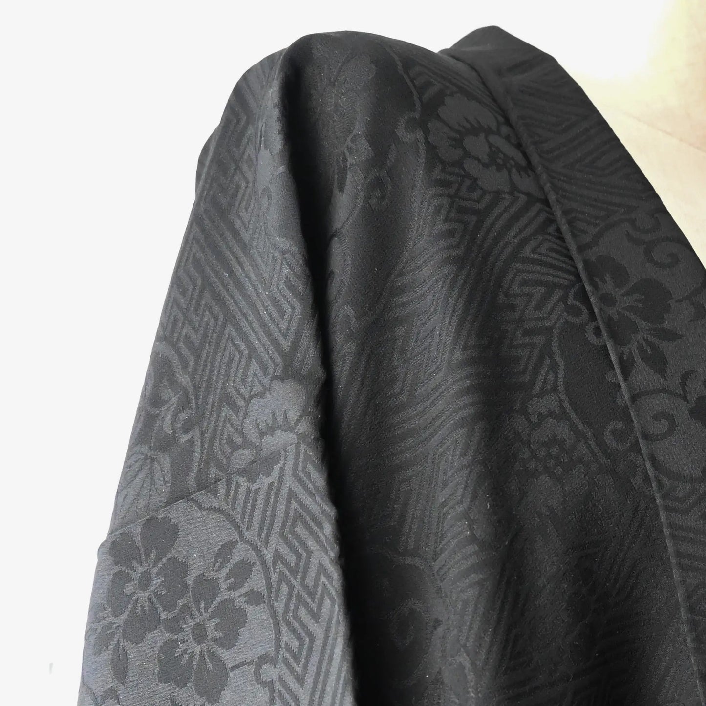 Detailed view of vintage women's black rinzu silk semi-formal haori with red silk lining.