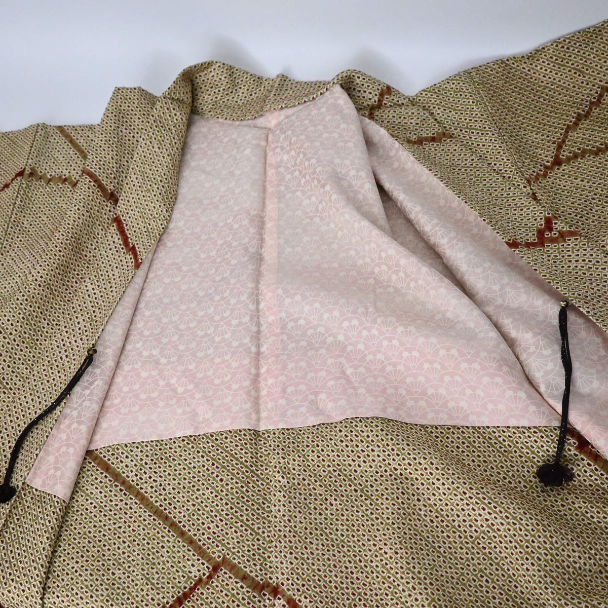 The lining of vintage women's silk shibori haori with an olive green and reddish-brown all-over pattern.