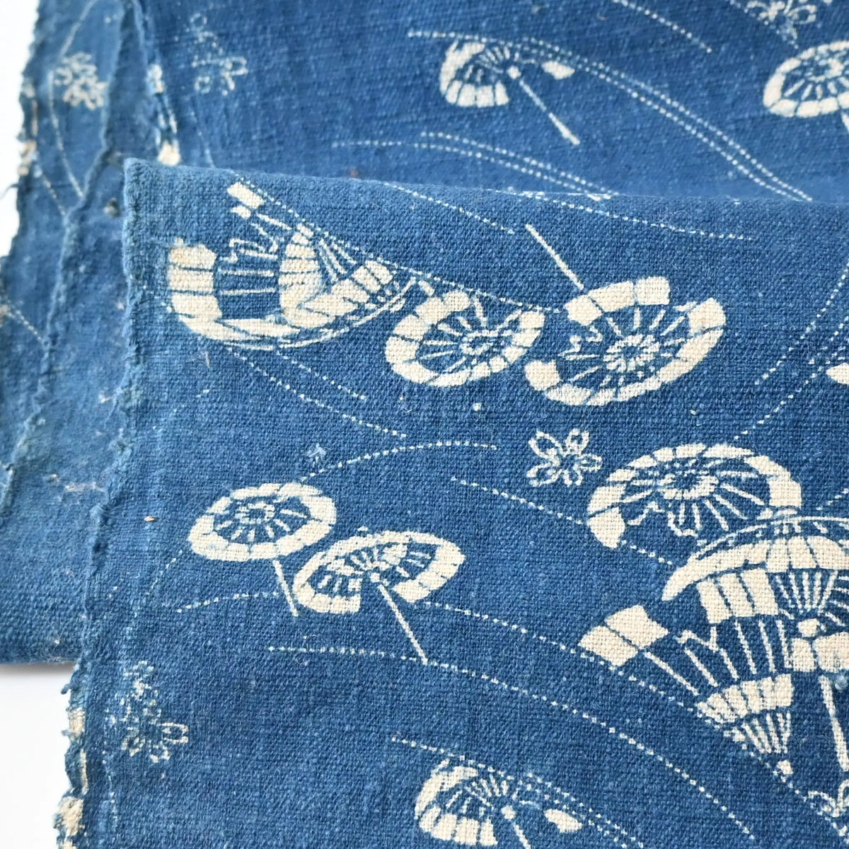 Close-up view of antique indigo katazome cotton with flowing wagasa (Japanese paper umbrellas) and cherry blossom motifs.