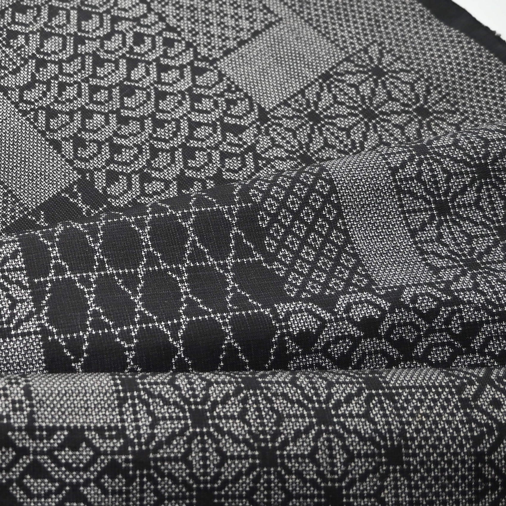Close-up view of vintage black silk kimono fabric roll with patchwork-style geometric pattern, sold by the metre.