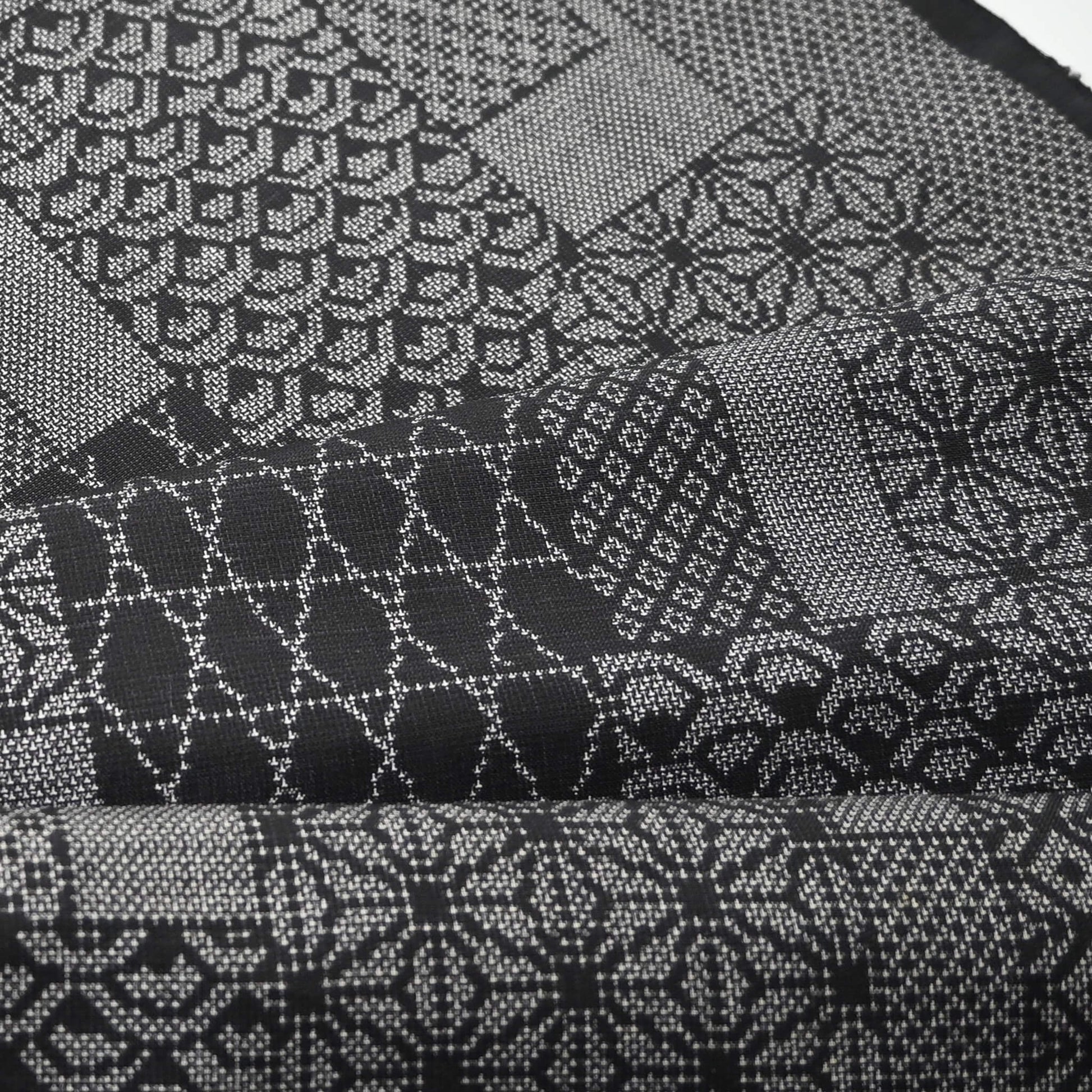 Close-up view of vintage black silk kimono fabric roll with patchwork-style geometric pattern, sold by the metre.