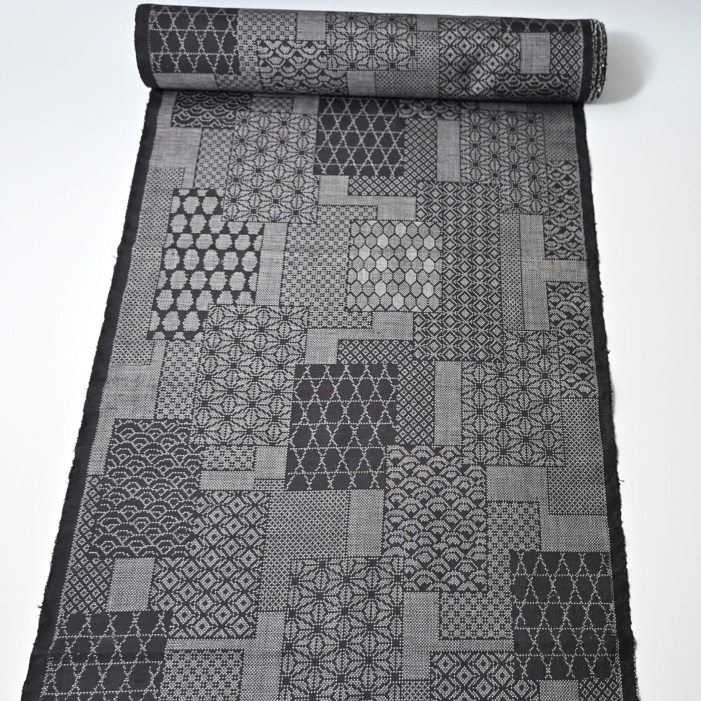 Full view of vintage black silk kimono fabric roll with patchwork-style geometric pattern, sold by the metre.