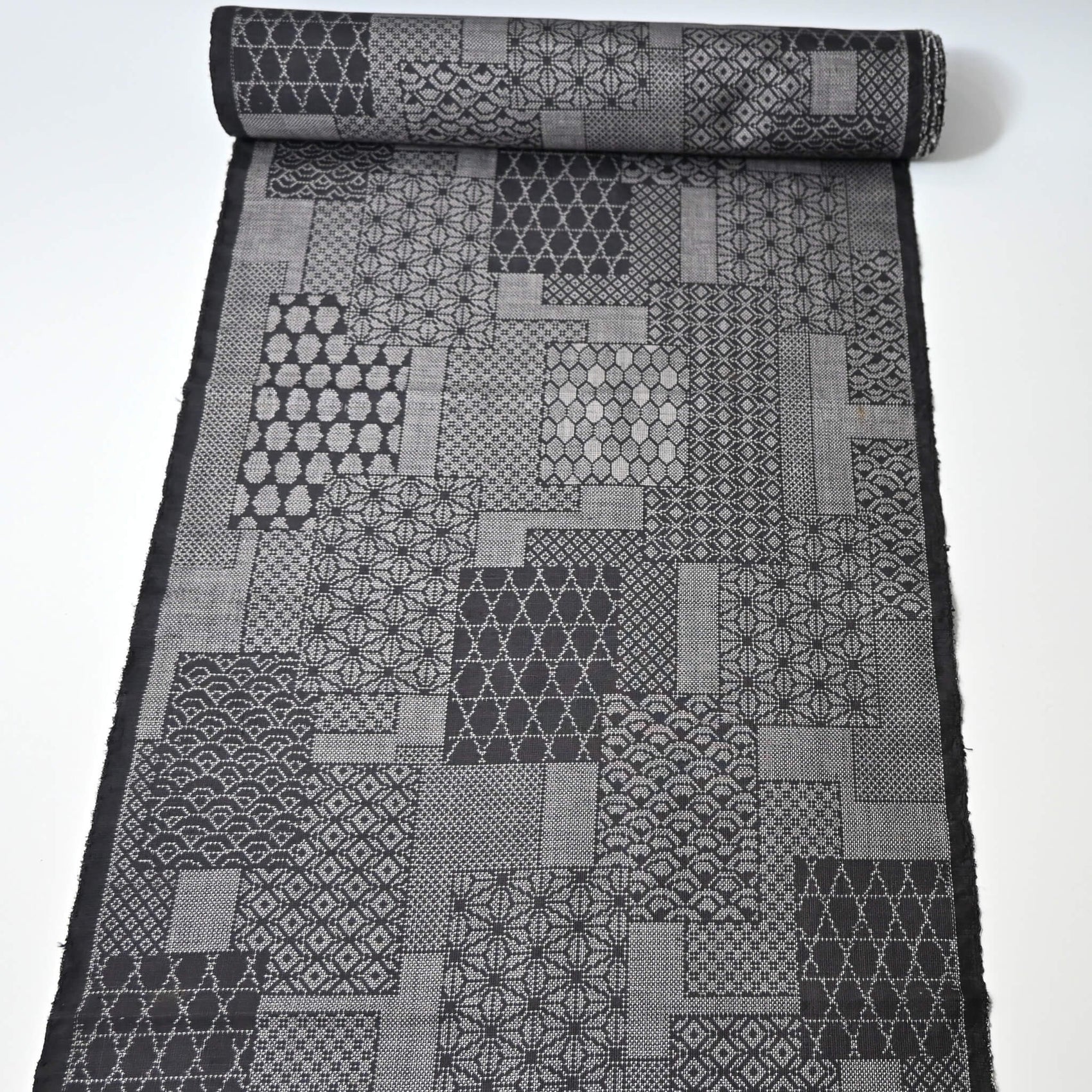 Full view of vintage black silk kimono fabric roll with patchwork-style geometric pattern, sold by the metre.