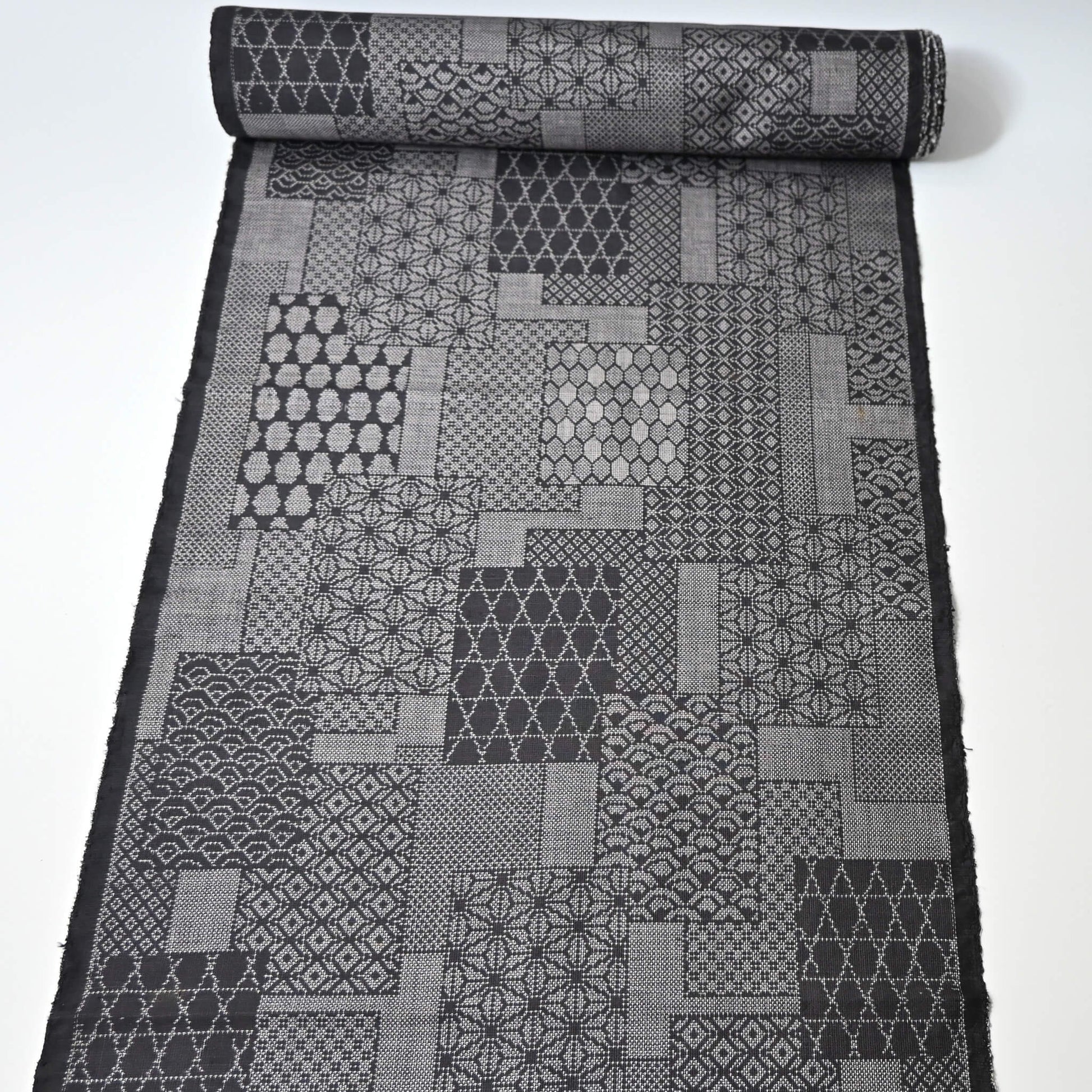 Full view of vintage black silk kimono fabric roll with patchwork-style geometric pattern, sold by the metre.