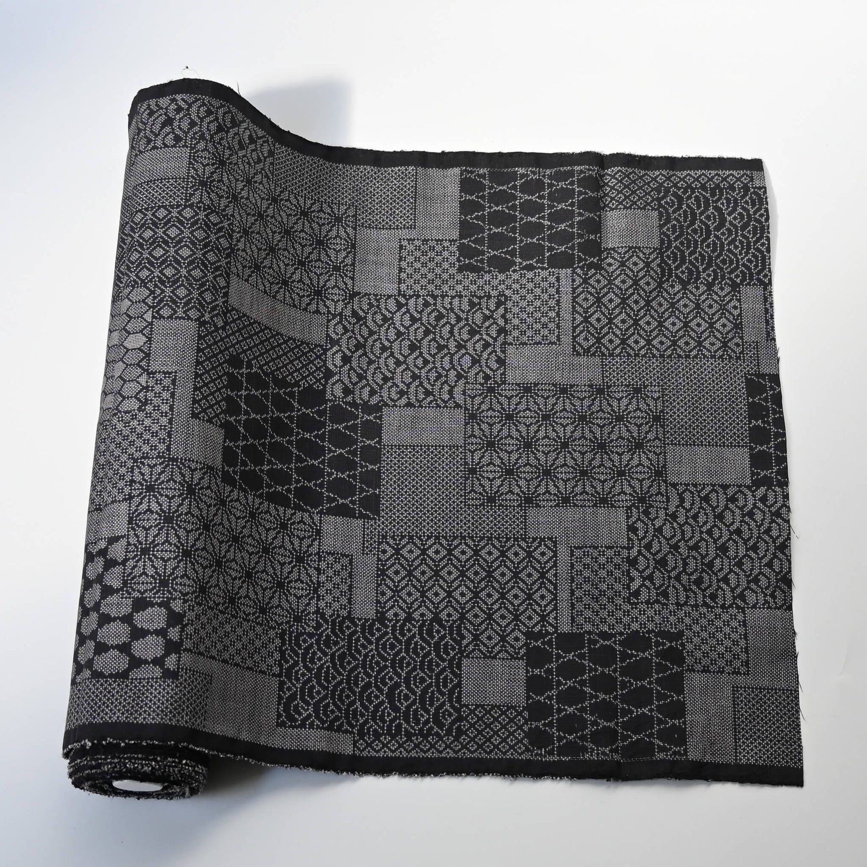 Vintage black silk kimono fabric roll with patchwork-style geometric pattern, sold by the metre.