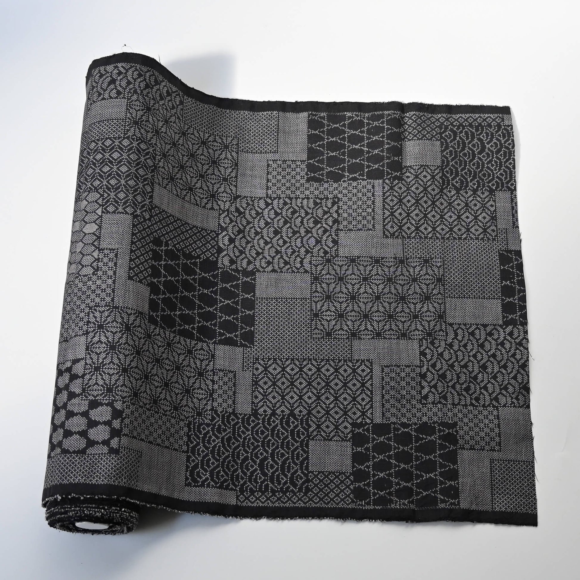 Vintage black silk kimono fabric roll with patchwork-style geometric pattern, sold by the metre.