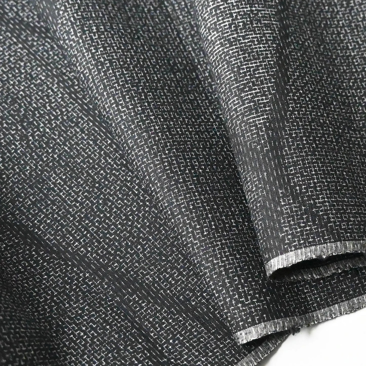 Detailed view of vintage black tsumugi silk kimono fabric roll with modern geometric pattern.