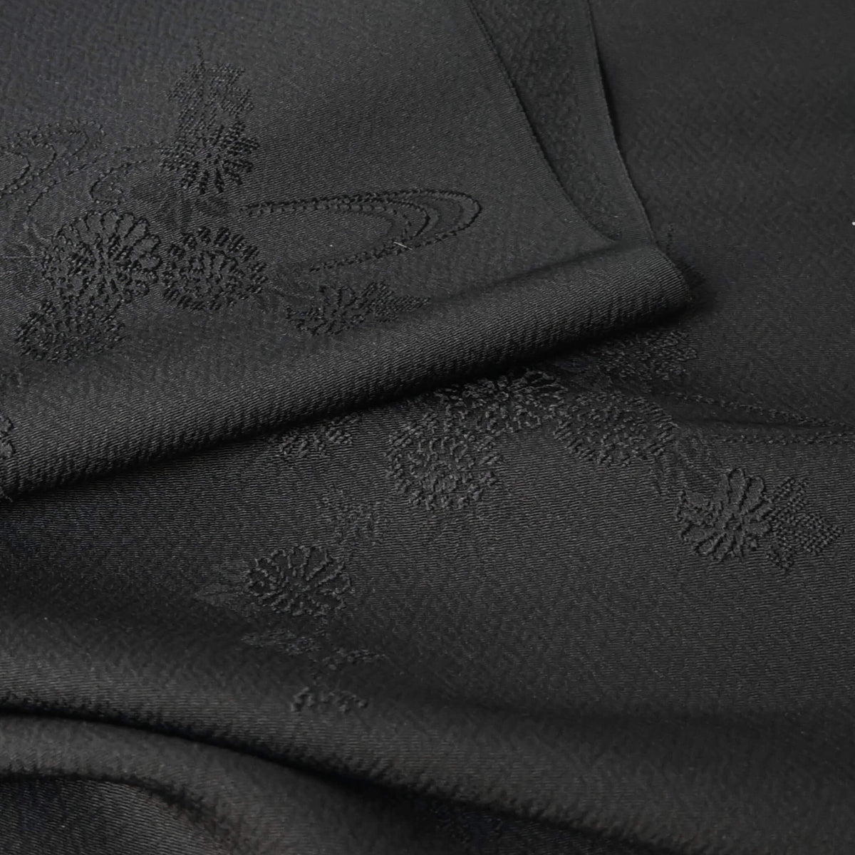 Close-up view of vintage black silk jacquard kimono fabric with running water and chrysanthemum motifs, drape well.