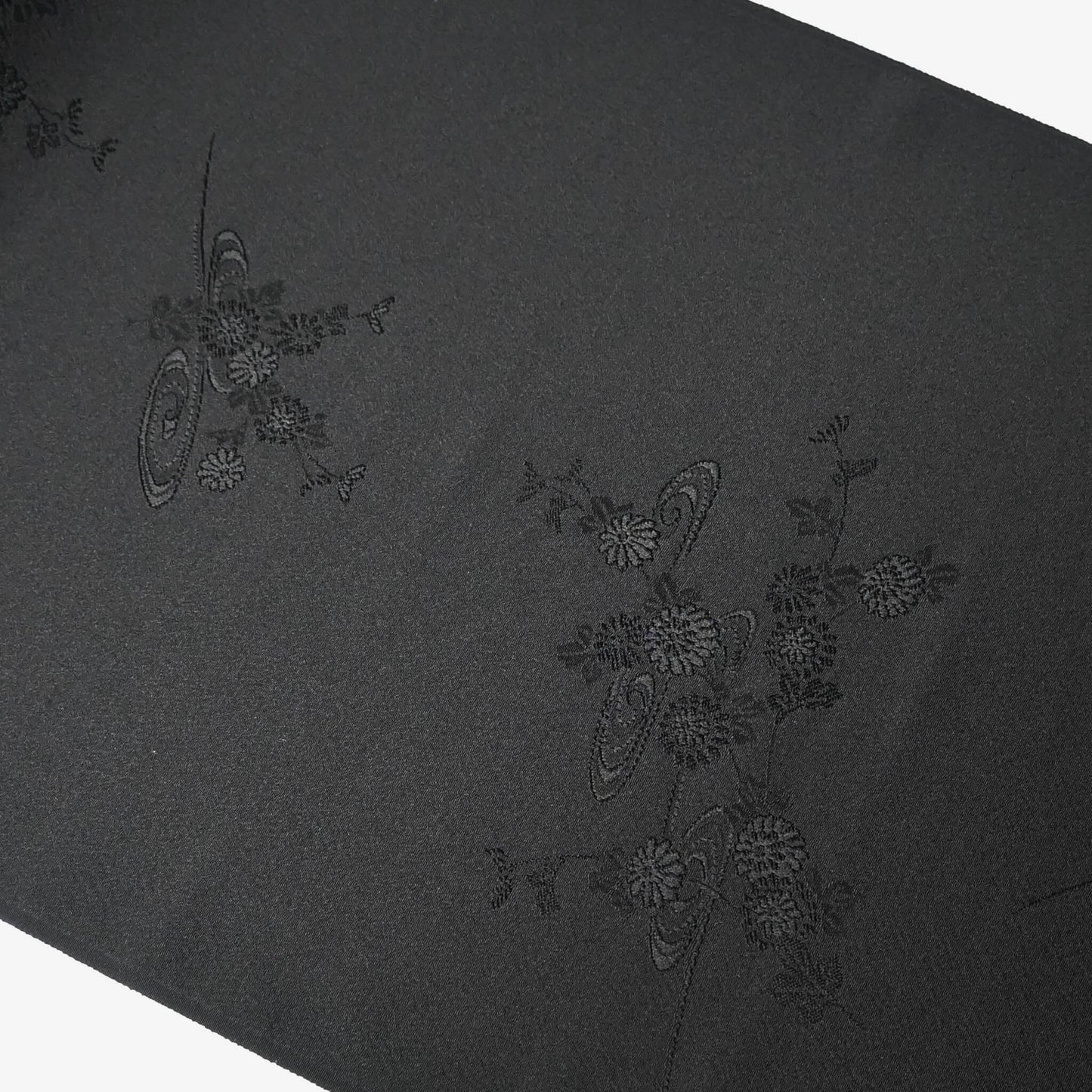 Detailed view of vintage black silk jacquard kimono fabric with running water and chrysanthemum motifs, drape well.