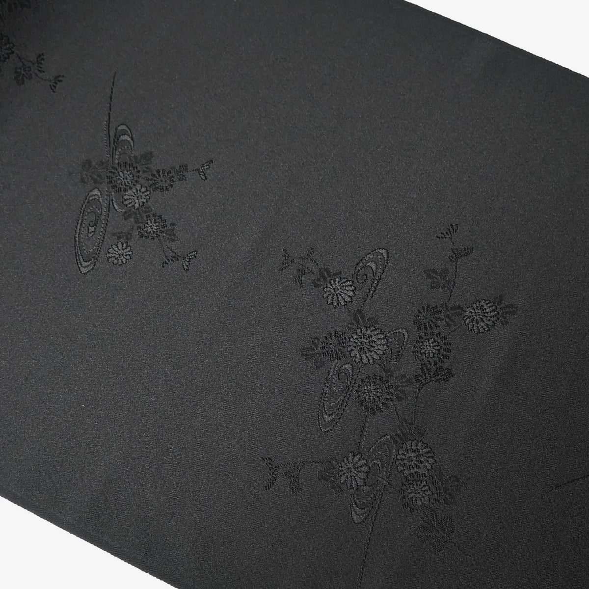 Detailed view of vintage black silk jacquard kimono fabric with running water and chrysanthemum motifs, drape well.