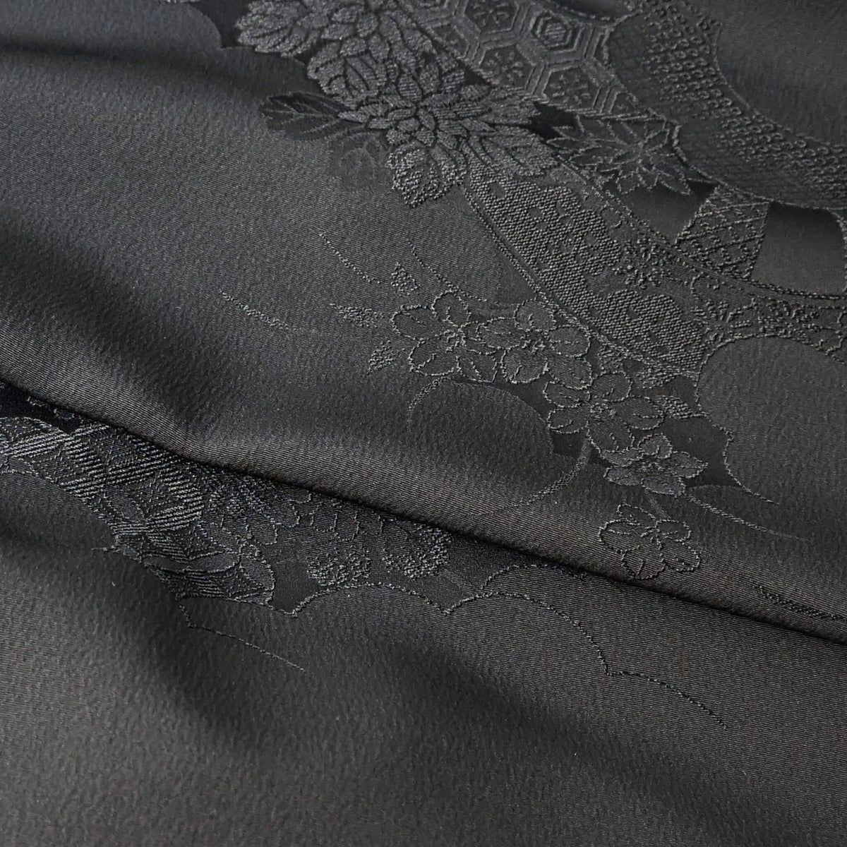 Close-up view of vintage Japanese black silk jacquard kimono fabric with floral motif, has a soft handle and drapes well.