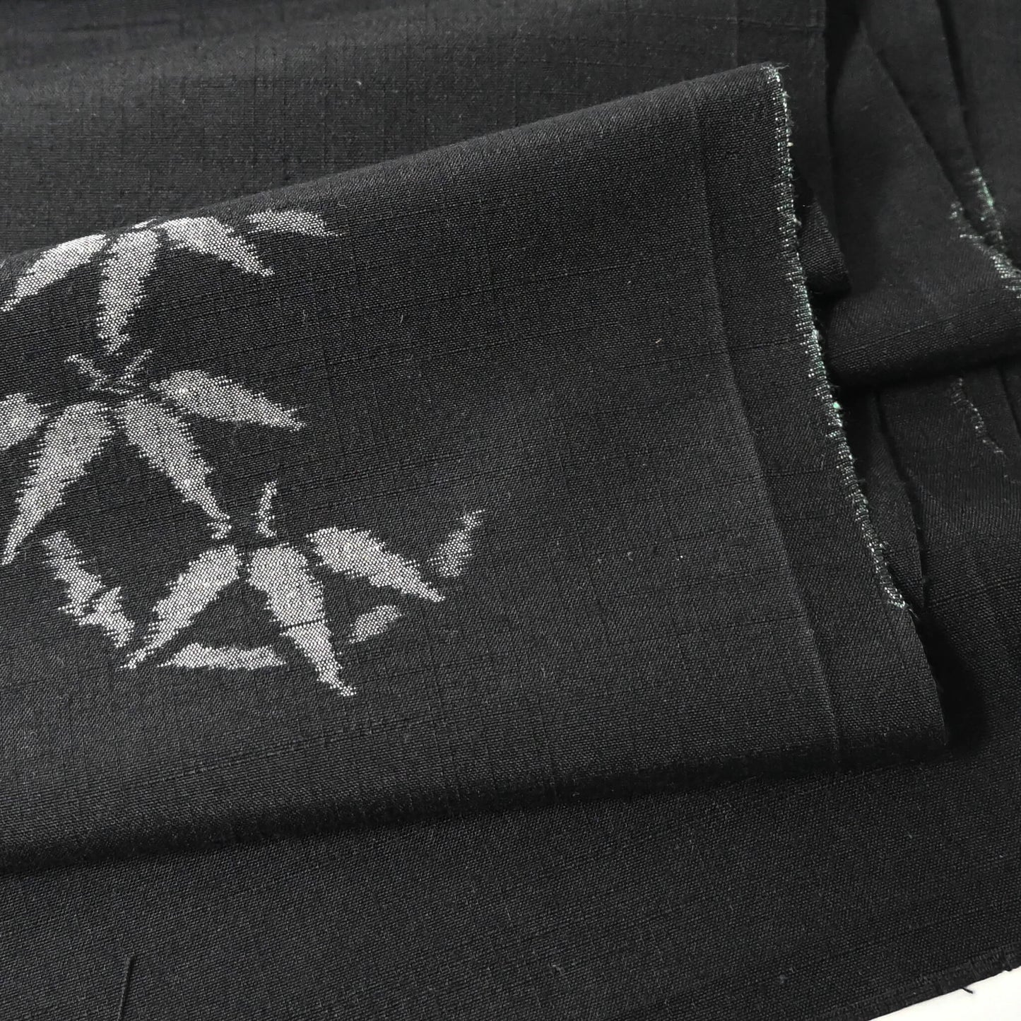 Close-up view of vintage Japanese tsumugi silk kimono fabric piece in black with small grey bamboo motif.