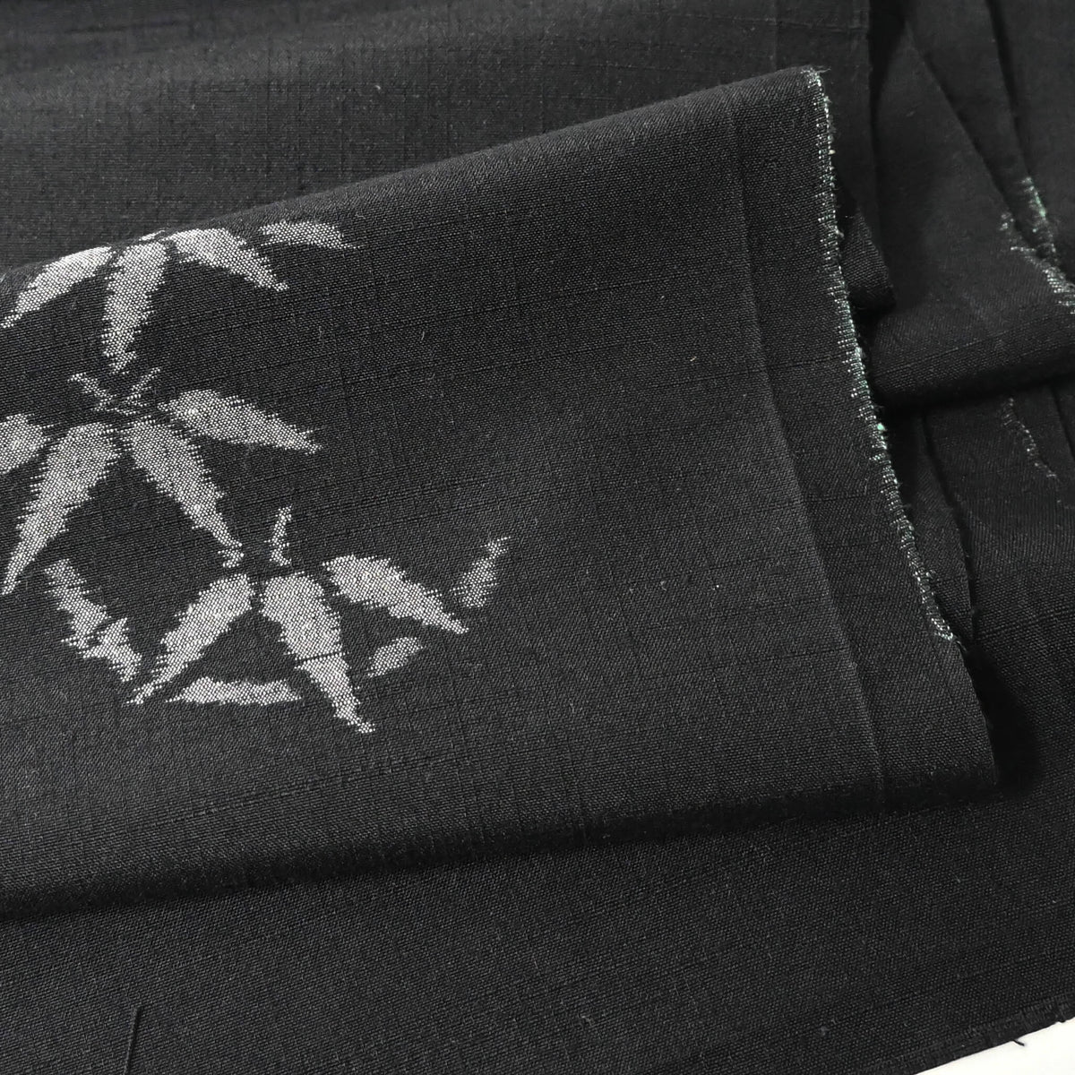 Close-up view of vintage Japanese tsumugi silk kimono fabric piece in black with small grey bamboo motif.