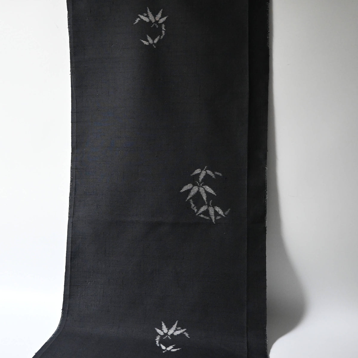 Hanging view of vintage Japanese tsumugi silk kimono fabric piece in black with small grey bamboo motif.
