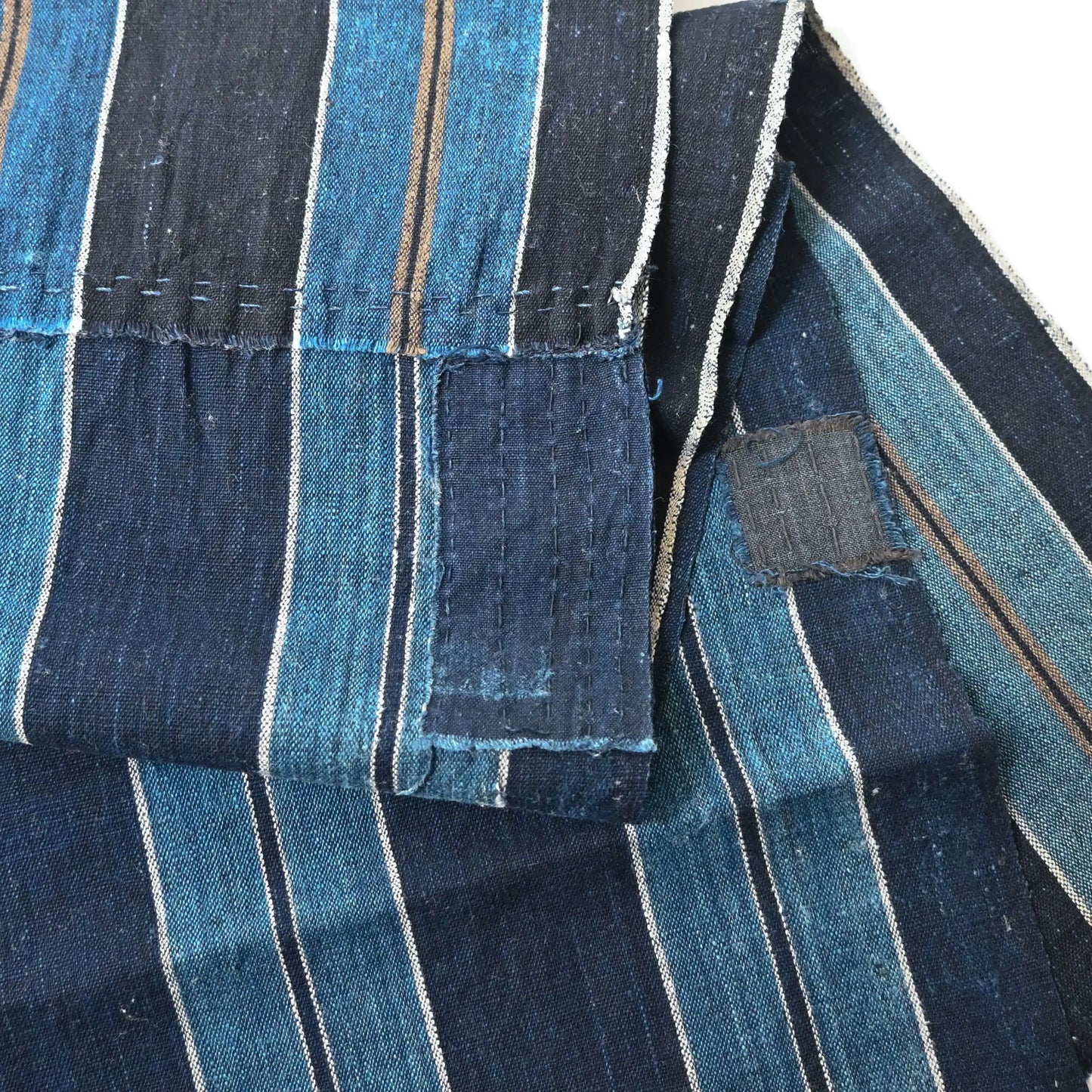 Close-up-view of vintage indigo stripe cotton from a futon cover,  two different stripe patterns joined together with mended patches.