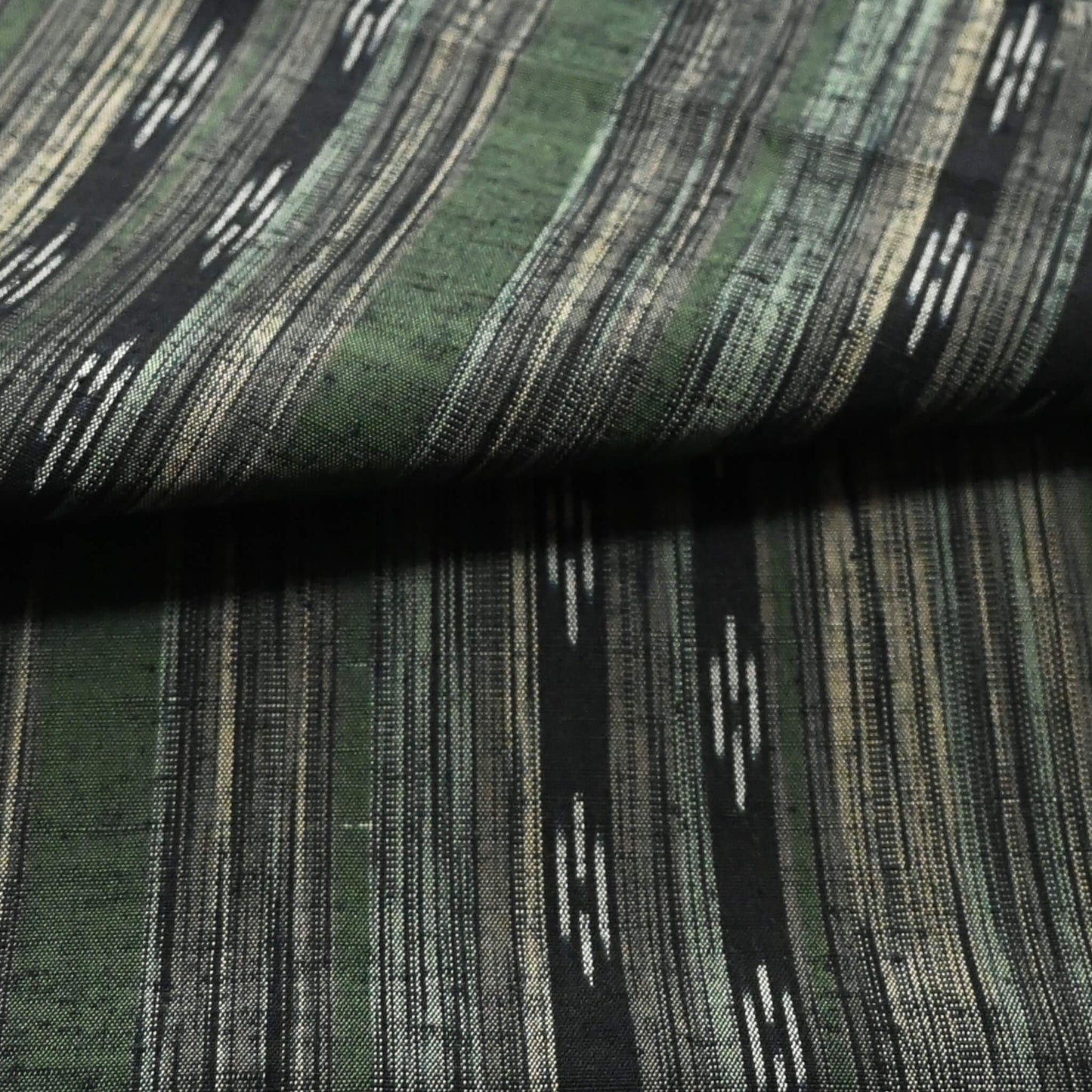 Close-up view of vintage tsumugi silk kimono fabric with olive green, charcoal and black stripes, and kasuri accents.