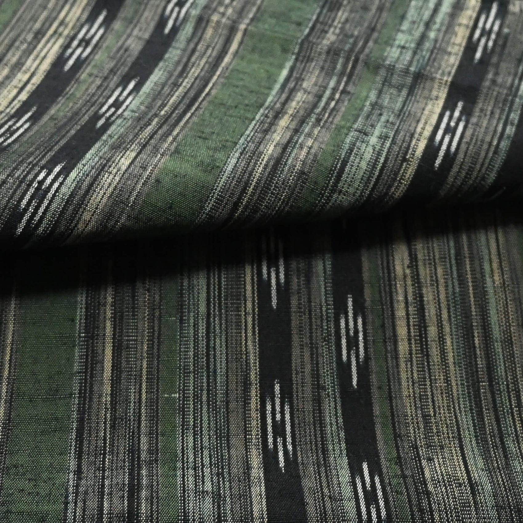 Close-up view of vintage tsumugi silk kimono fabric with olive green, charcoal and black stripes, and kasuri accents.
