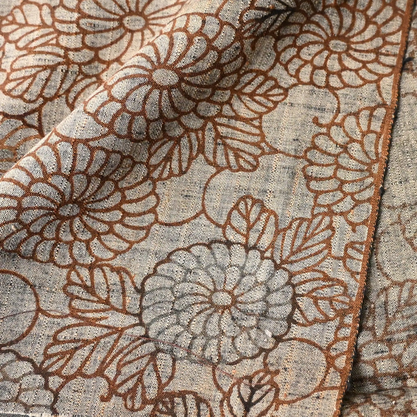 Close-up view of vintage tsumugi silk kimono fabric in earthy greige colour with brown chrysanthemum motif.