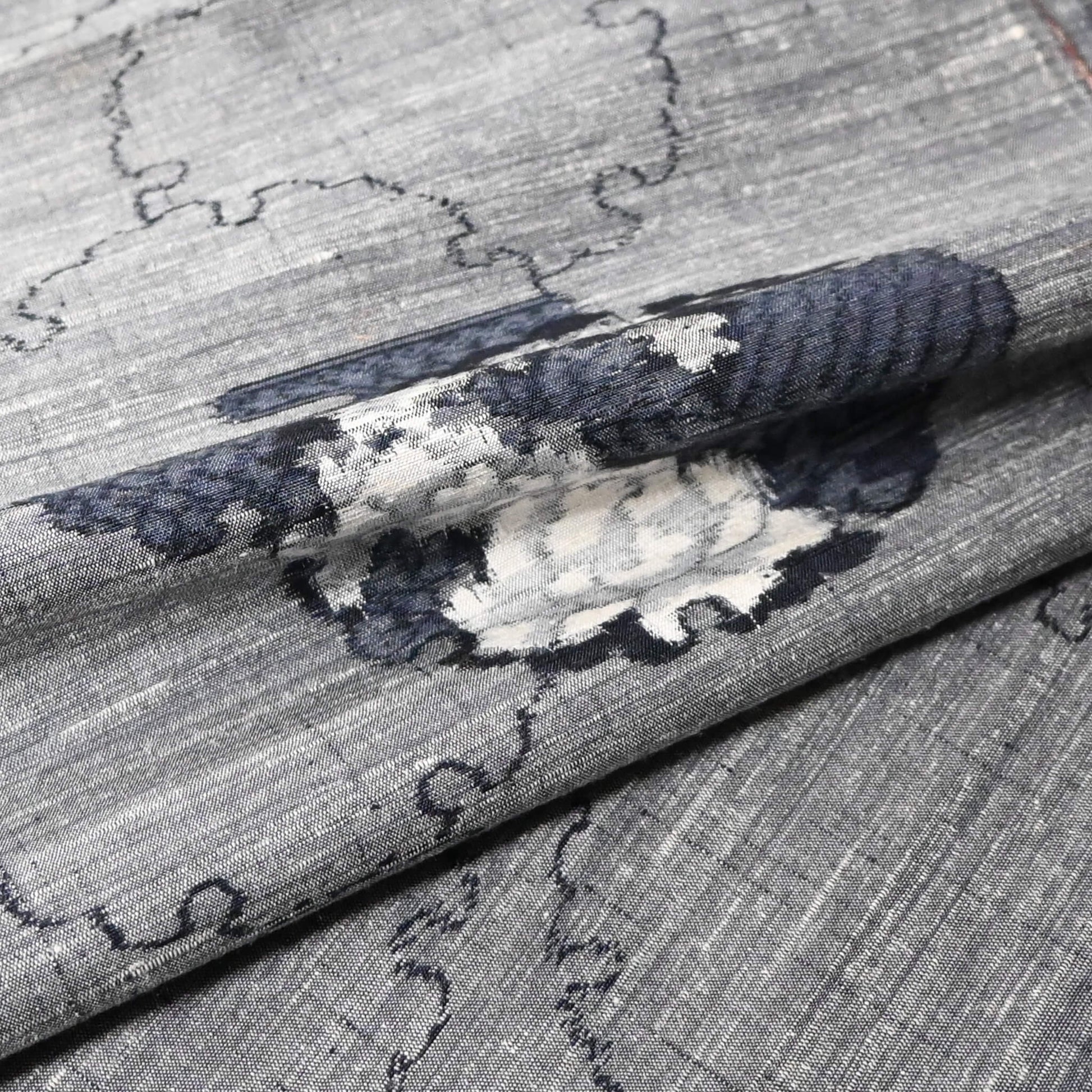 Close-up view of vintage grey tsumugi silk kimono fabric piece with floral pattern.