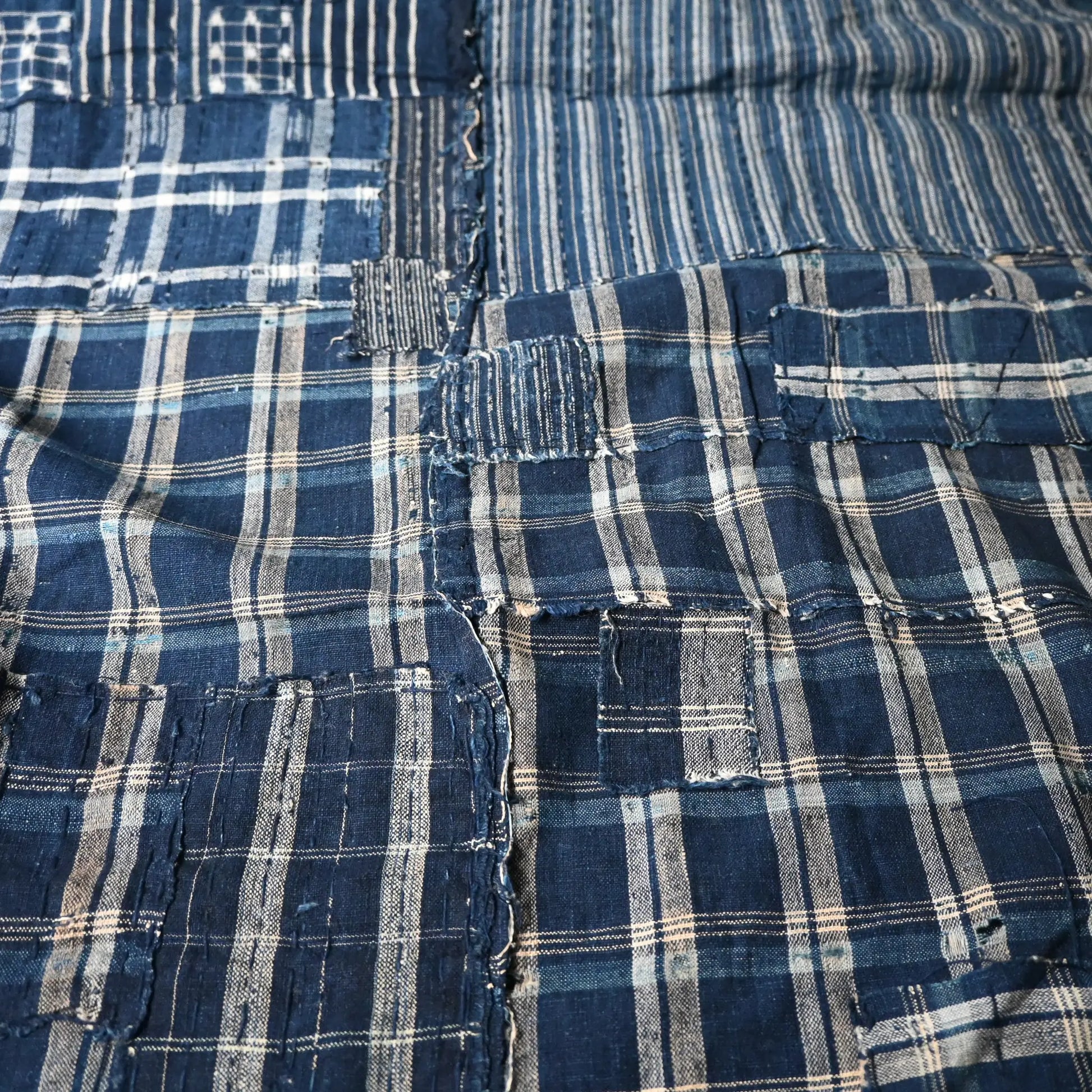 Detailed view of vintage Japanese indigo check cotton Boro futon cover with layers of mending.