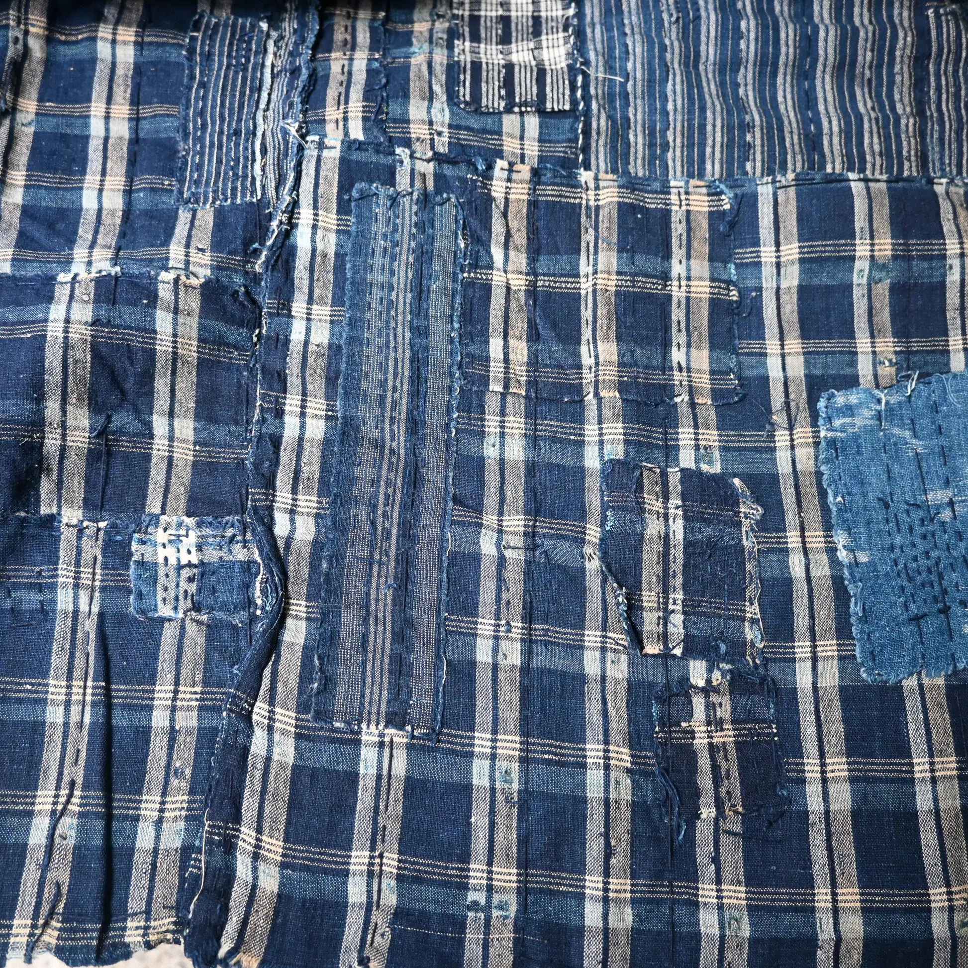 Detailed view of vintage Japanese indigo check cotton Boro futon cover with layers of mending.