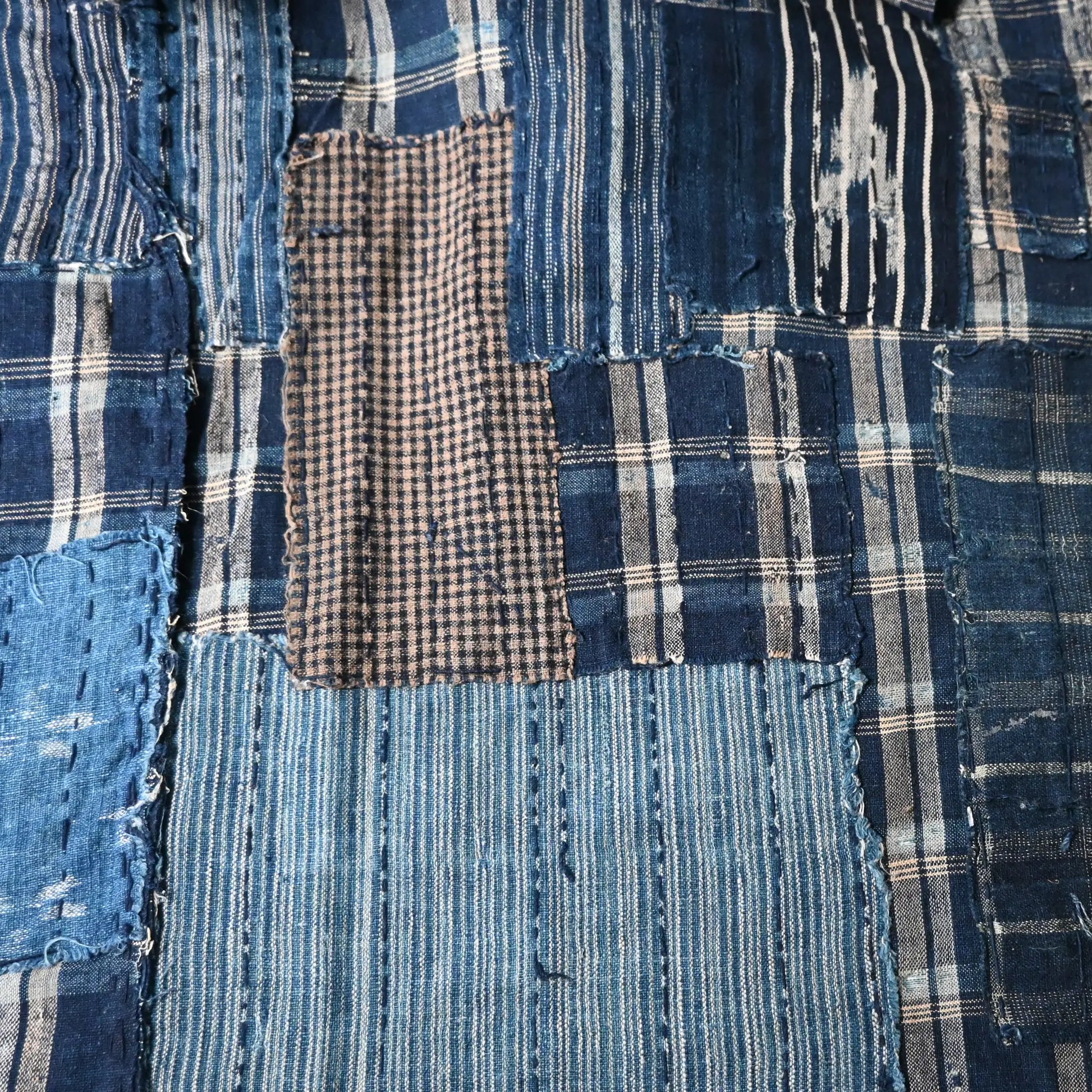 Detailed view of vintage Japanese indigo check cotton Boro futon cover with layers of mending.