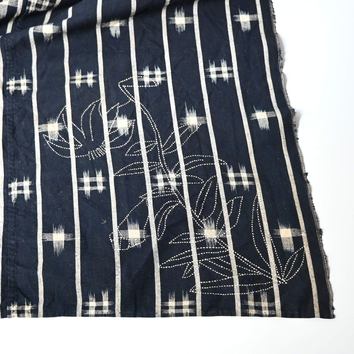 Detailed view of vintage three-panel indigo kasuri cotton furoshiki with hand stitched botanical motifs on the corner.