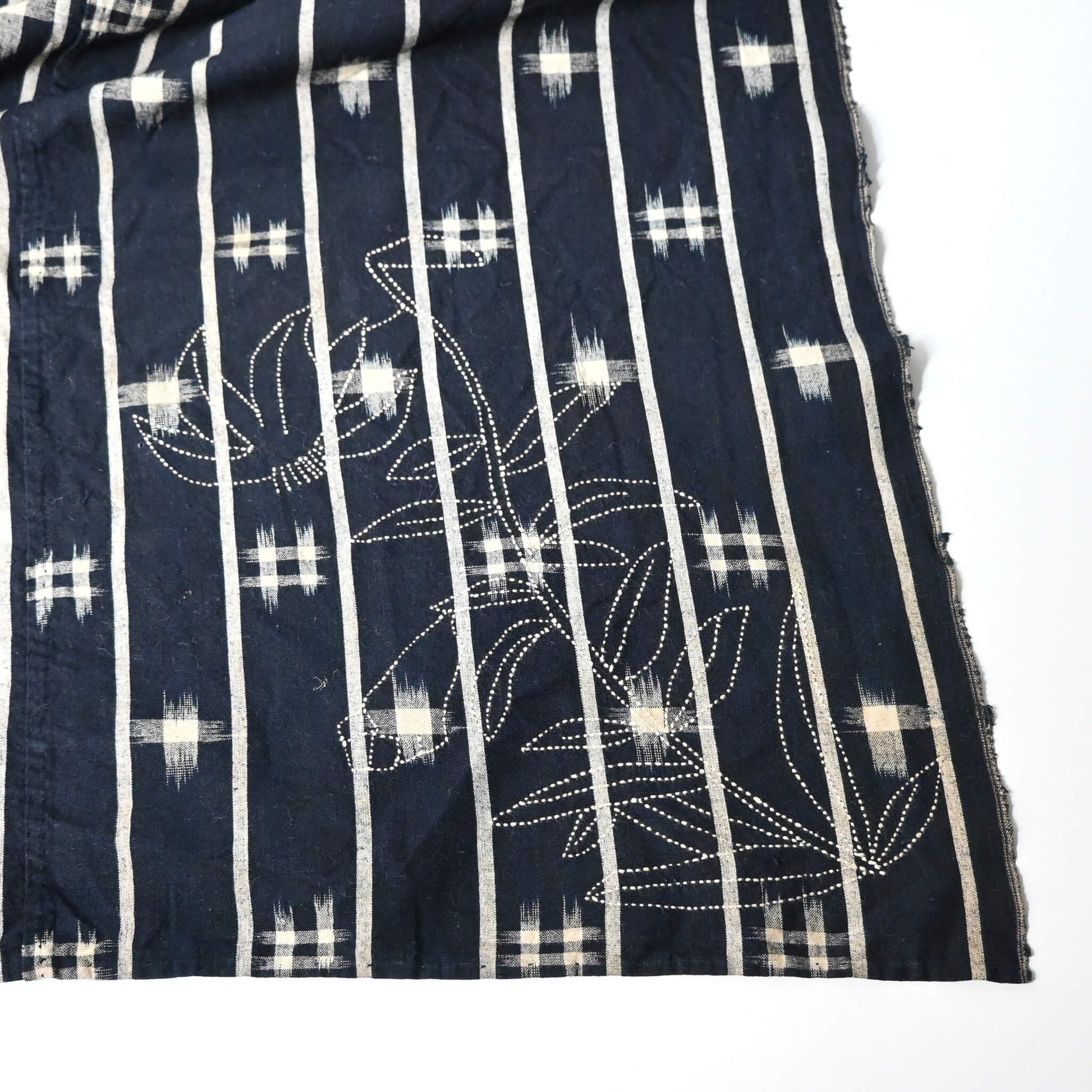 Detailed view of vintage three-panel indigo kasuri cotton furoshiki with hand stitched botanical motifs on the corner.