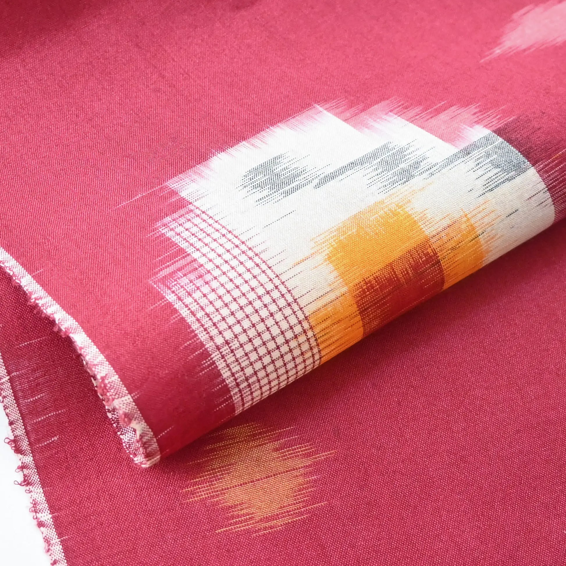 Detailed view of vintage Japanese kasuri cotton kimono fabric roll in raspberry pink with a bold pattern from the mid 20th century.