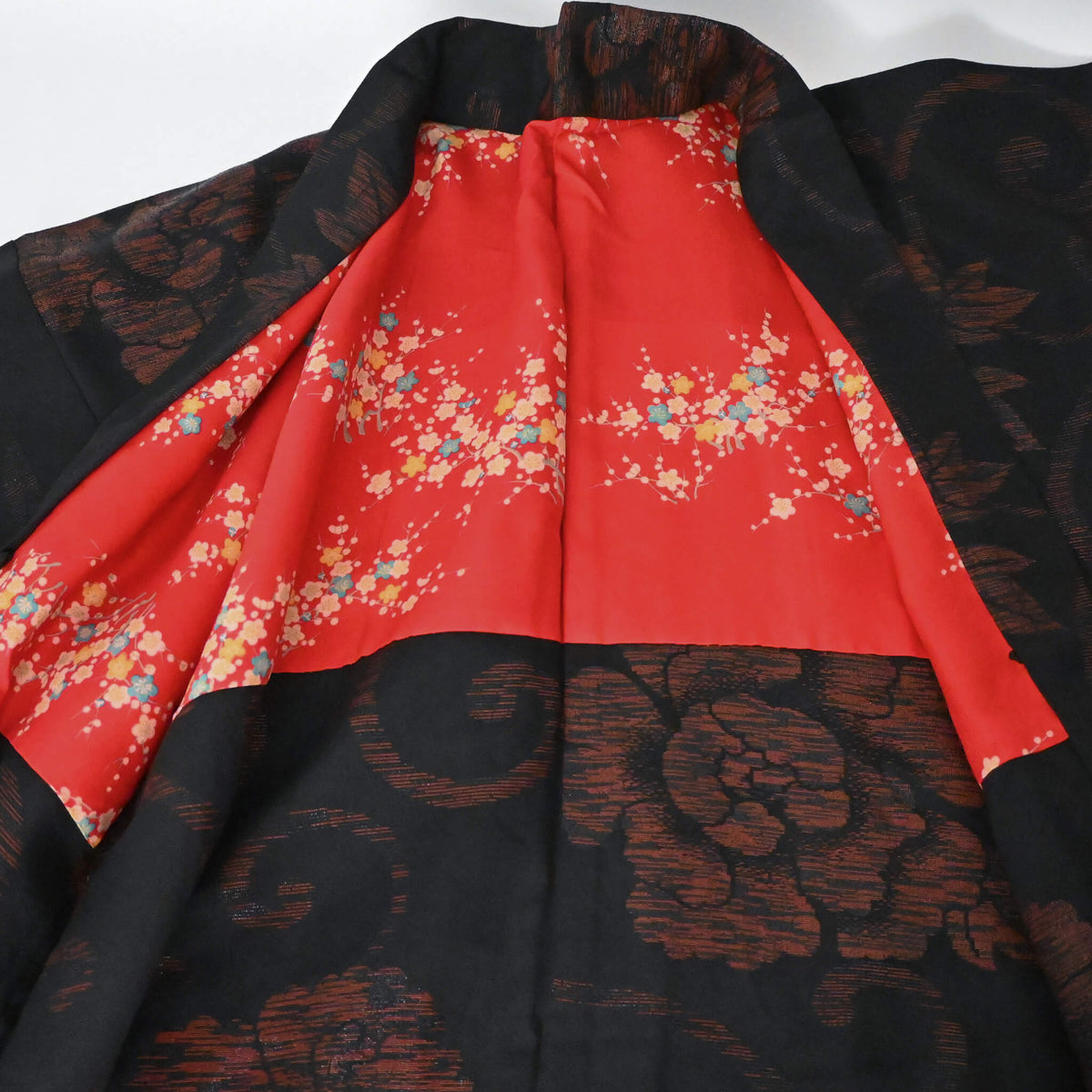 Vintage women's black silk crepe haori with woven peony pattern has a bright red silk lining.