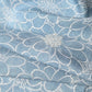 Close-up view of vintage light blue tsumugi silk kimono fabric with chrysanthemum motifs and shibori accents.