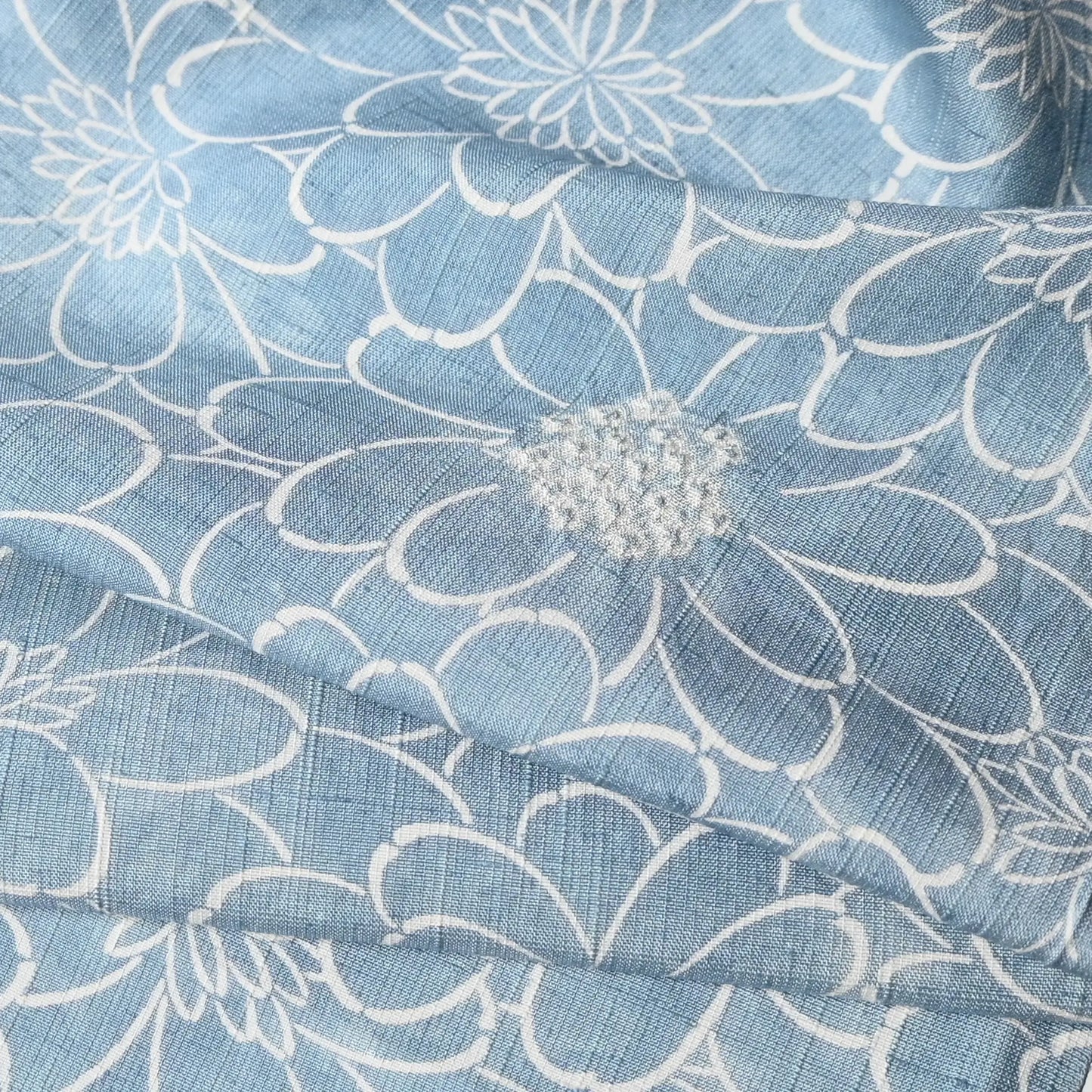 Close-up view of vintage light blue tsumugi silk kimono fabric with chrysanthemum motifs and shibori accents.