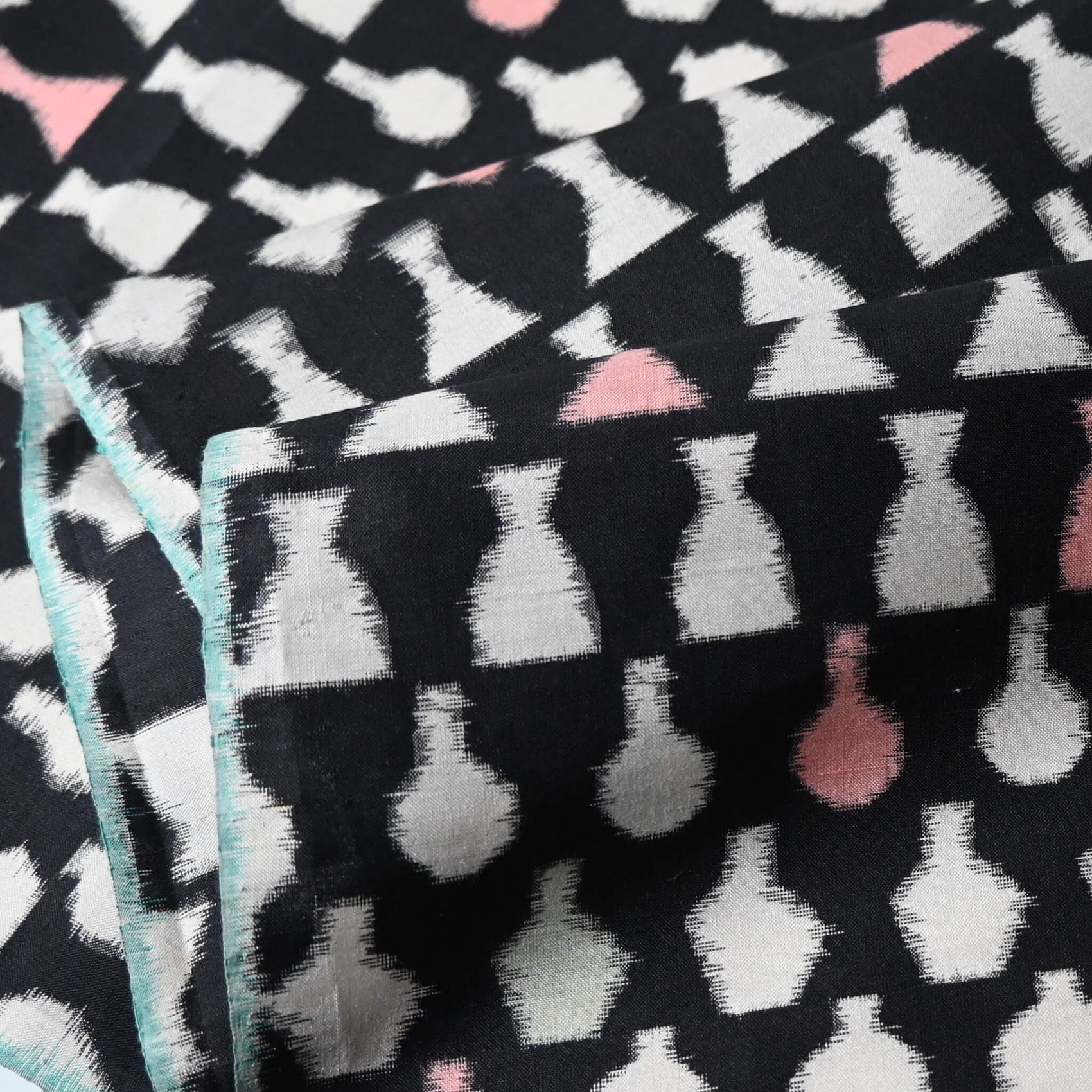 Close-up view of vintage Meisen silk kimono fabric piece, stylised vase motif in white and pink against black.