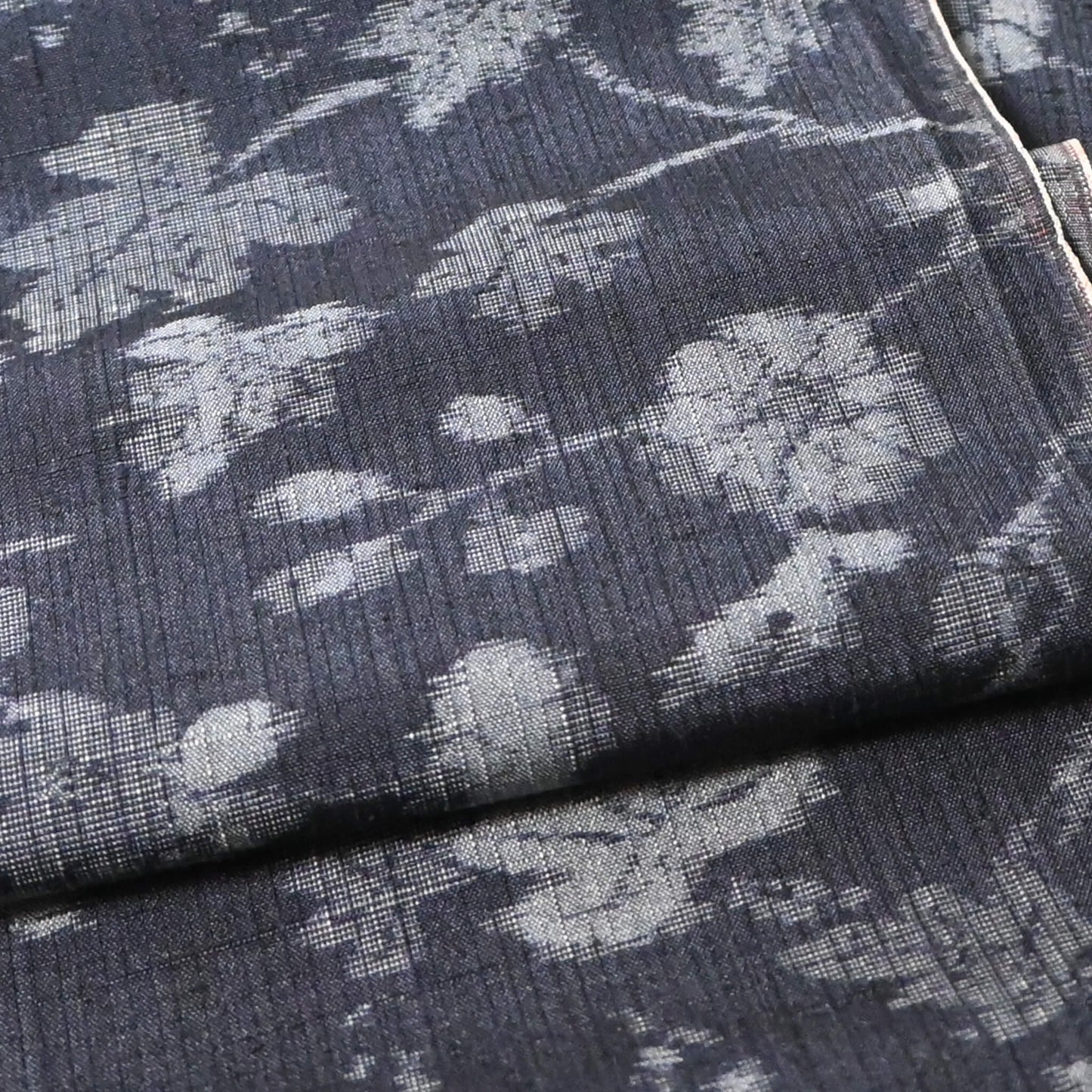 Close-up view of vintage tsumugi silk kimono fabric with silver grey vine floral pattern on a navy ground.