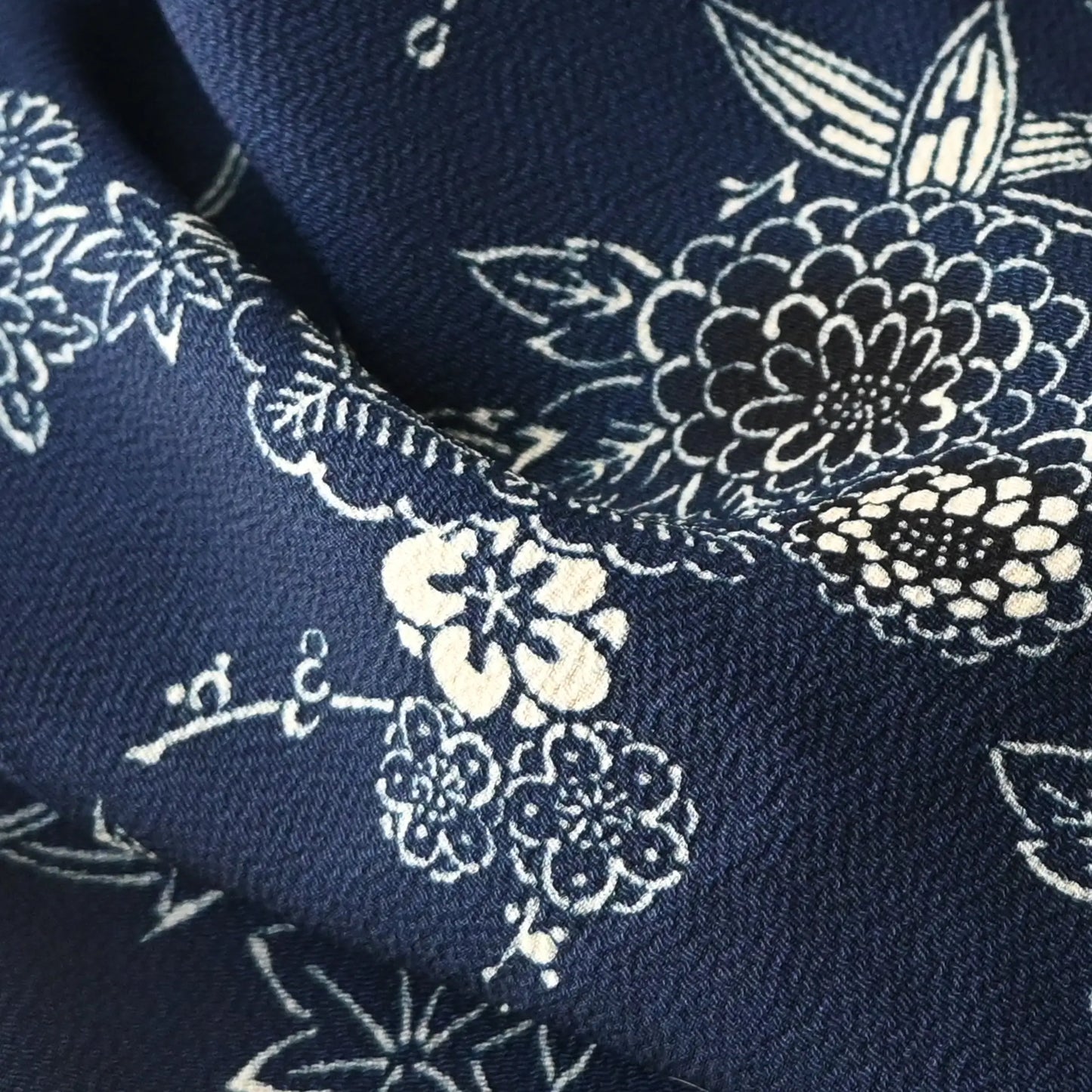 Close-up view of vintage Chirimen  silk crepe kimono fabric in navy with traditional Japanese seasonal flowers and trees.