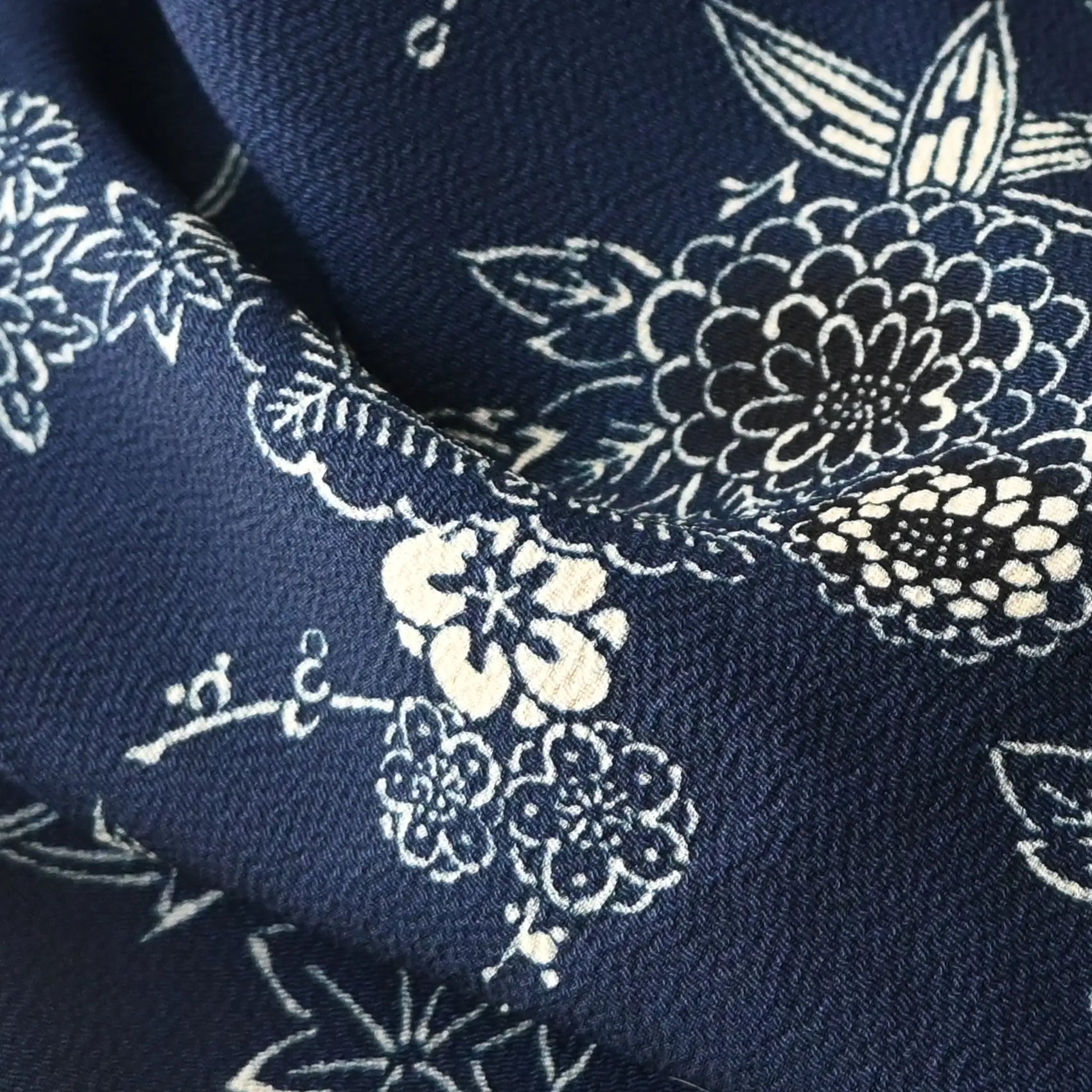 Close-up view of vintage Chirimen  silk crepe kimono fabric in navy with traditional Japanese seasonal flowers and trees.