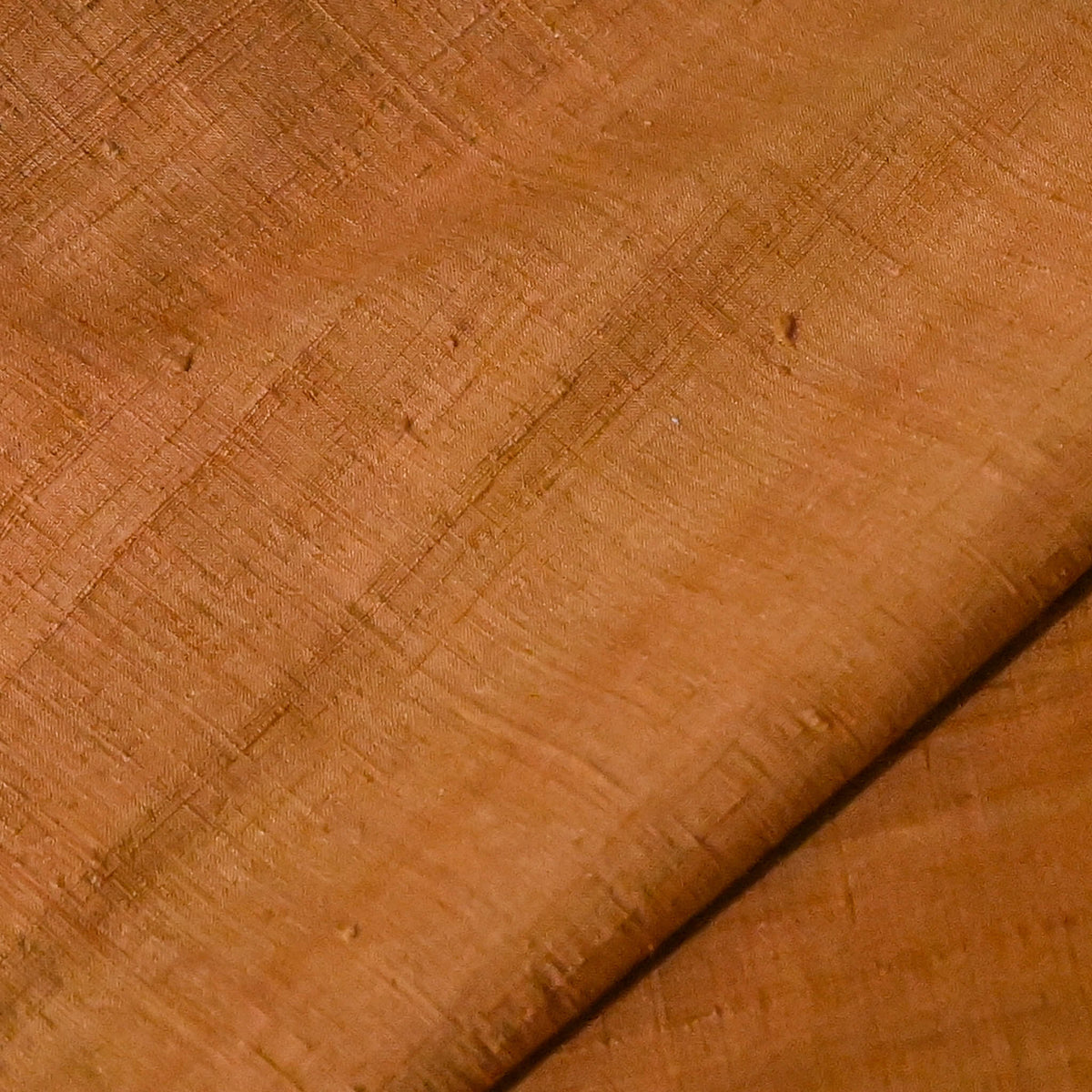 Close-up view of vintage plain tsumugi silk kimono fabric piece in warm ochre tone with slub texture.