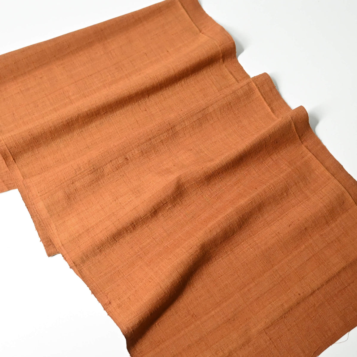 Full view of vintage plain tsumugi silk kimono fabric piece in warm ochre tone with slub texture.