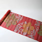 Laid view of vintage Japanese red ro silk obi fabric, showcasing bold lily and bellflower.