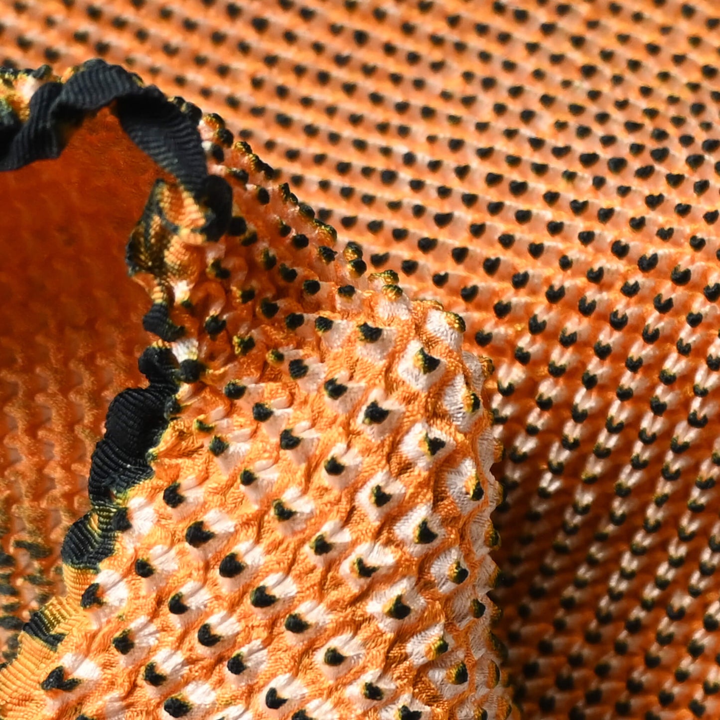 Close-up view of vintage silk shibori kimono fabric bolt in orange and black, unfinished, yunoshimae.