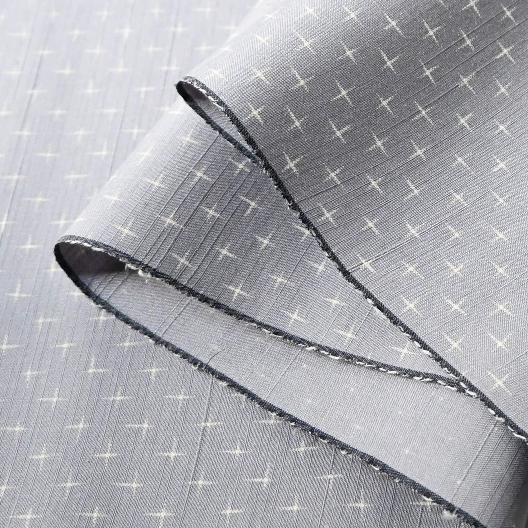 Close-up view of vintage tsumugi silk kimono fabric sold by the metre in soft grey lilac tone with cross motif.