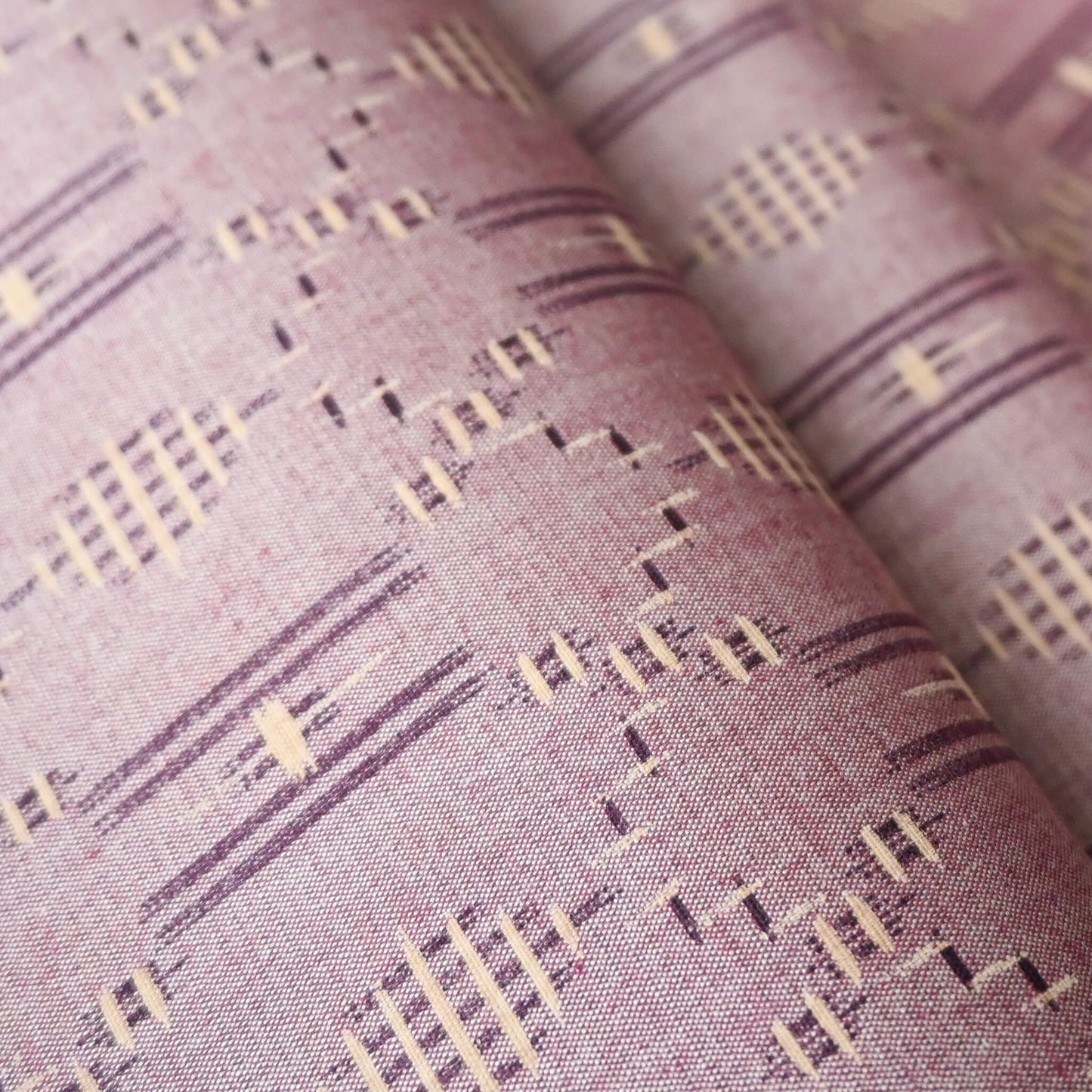 Close-up view of vintage mauve tsumugi silk kimono fabric roll with geometric pattern.