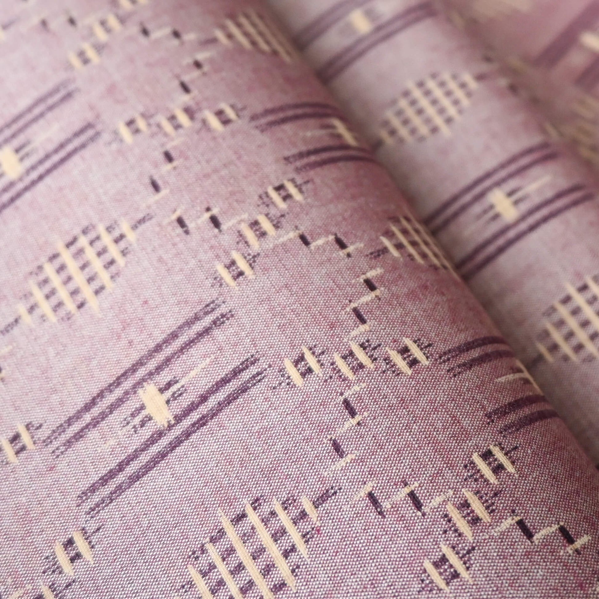 Close-up view of vintage mauve tsumugi silk kimono fabric roll with geometric pattern.