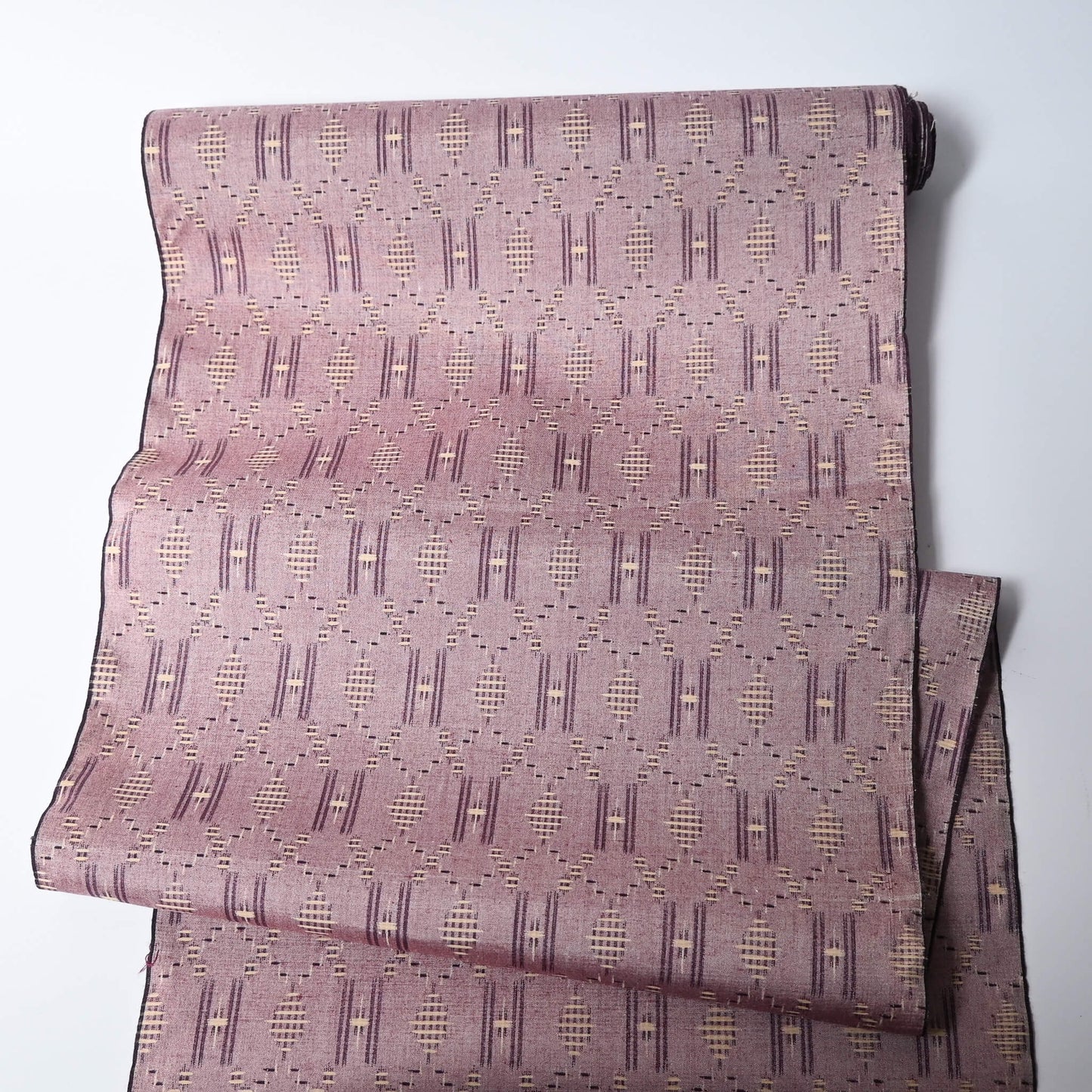 Full view of vintage mauve tsumugi silk kimono fabric roll with geometric pattern.