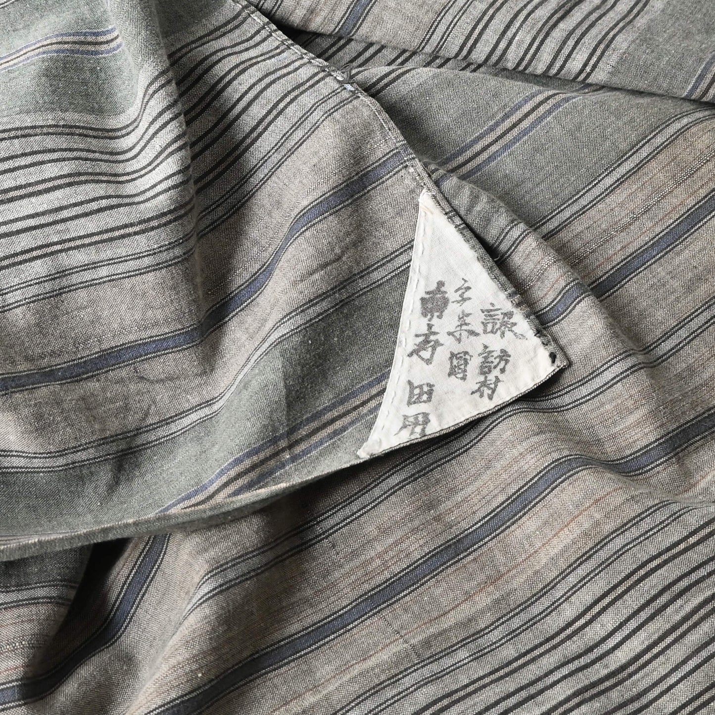 Detailed view of vintage stripe cotton furoshiki in soft grey tone, with some mended patches with indigo cottons.