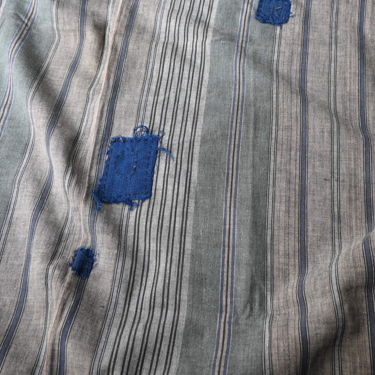 Detailed view of vintage stripe cotton furoshiki in soft grey tone, with some mended patches with indigo cottons.