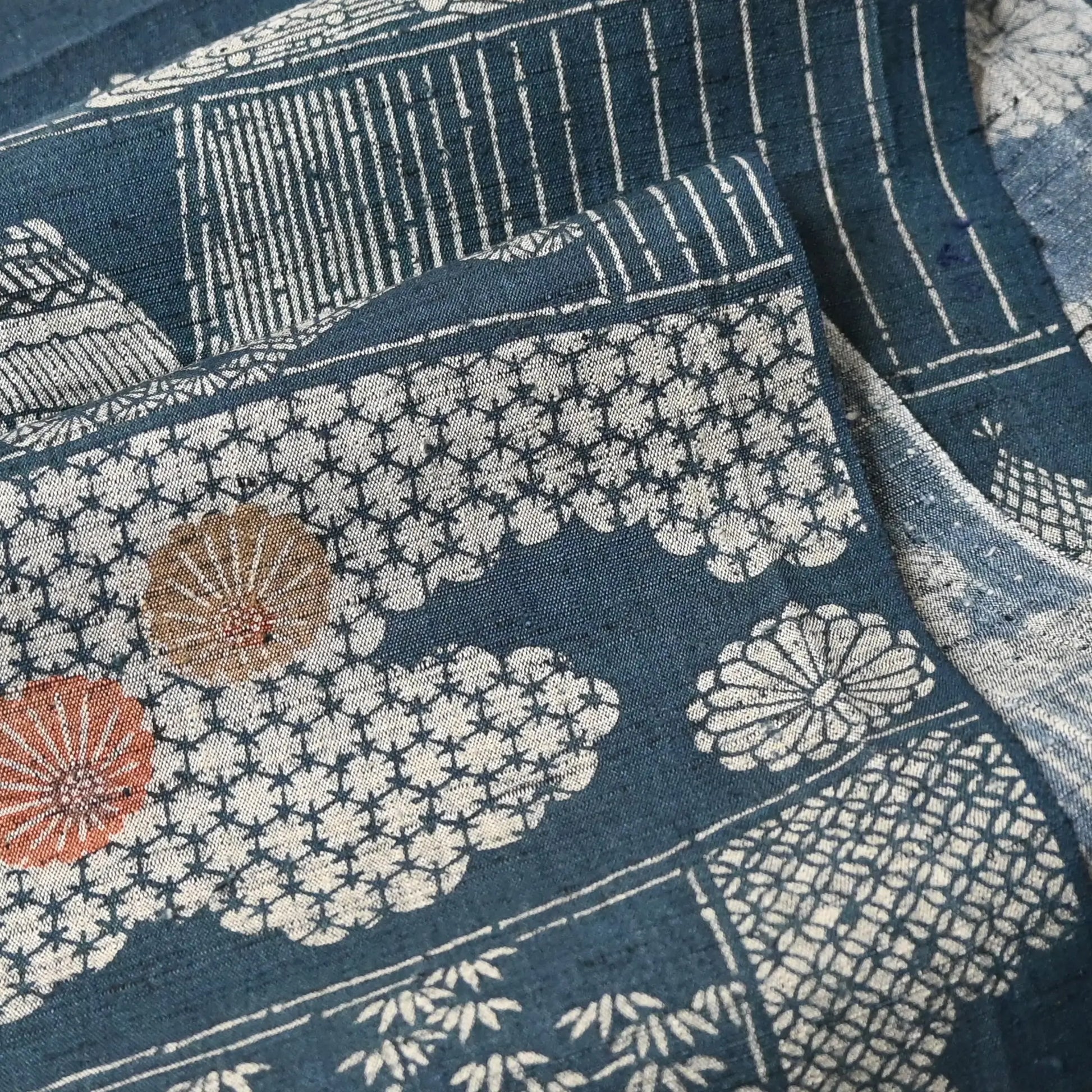 Close-up view of vintage muted blue tsumugi silk kimono fabric piece with houses and chrysanthemum accents.
