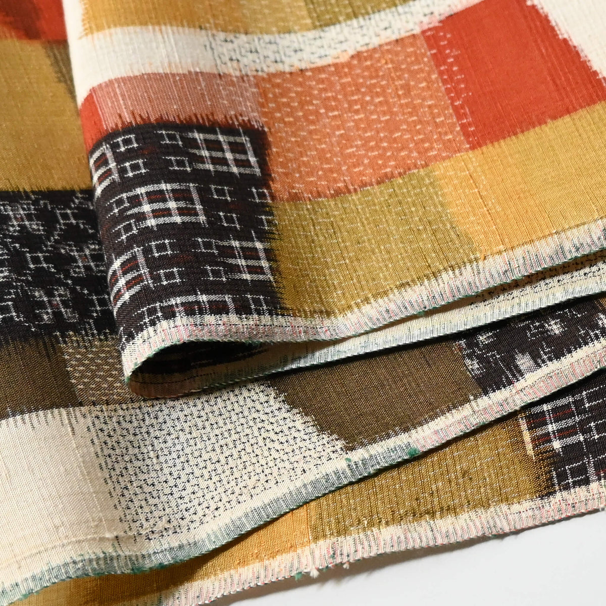 Close-up view of vintage textured tsumugi silk kimono fabric with  an abstract geometric design in warm shades.